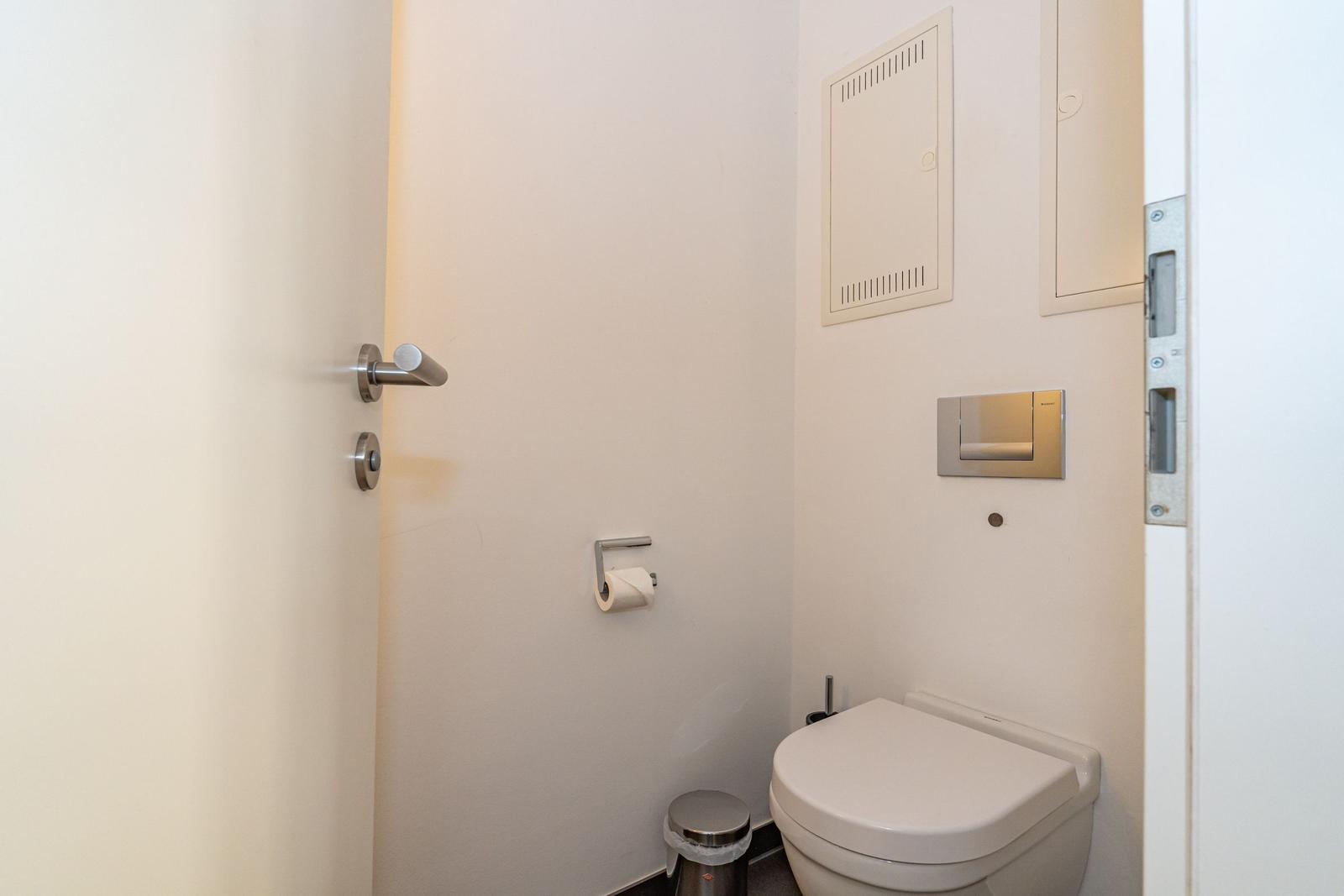 Toilettenraum mit Toilette, Toilettenpapierhalter und Metallmülleimer.
