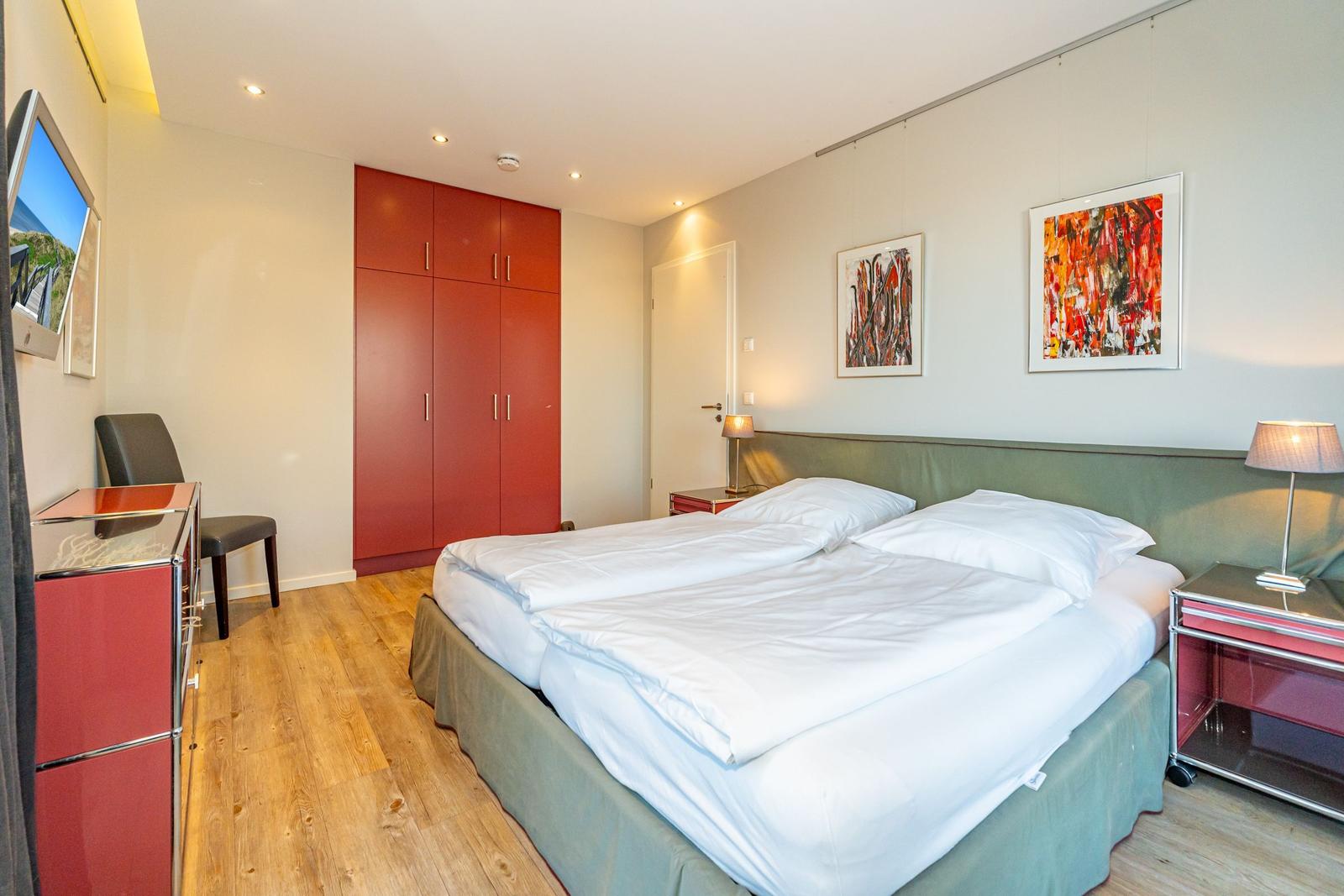Schlafzimmer mit Doppelbett, rotem Schrank und Holzboden.