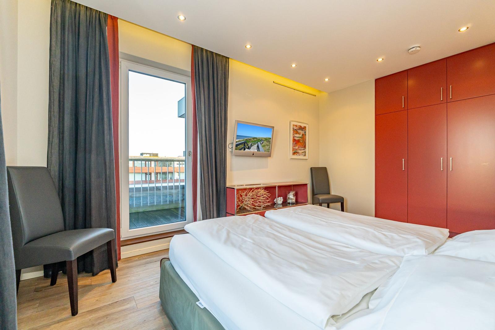 Schlafzimmer mit Doppelbett, rotem Schrank und Fenster zum Balkon.