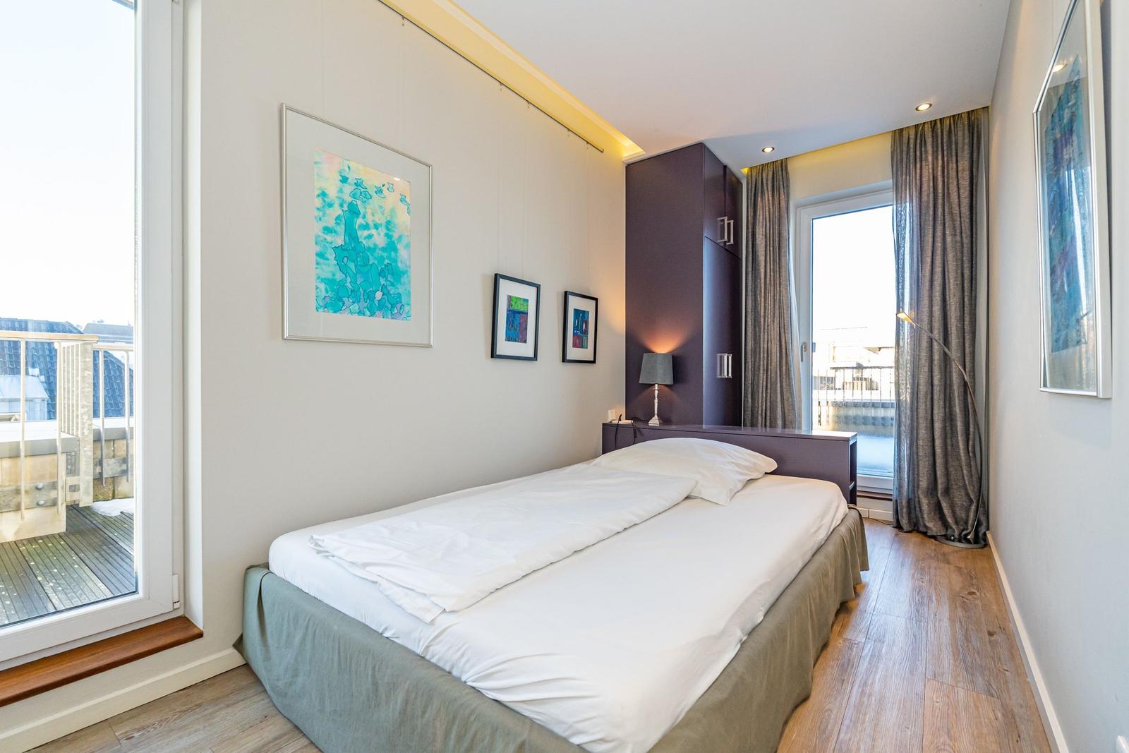 Schlafzimmer mit Bett, Fenster und Kunstwerken an den Wänden.
