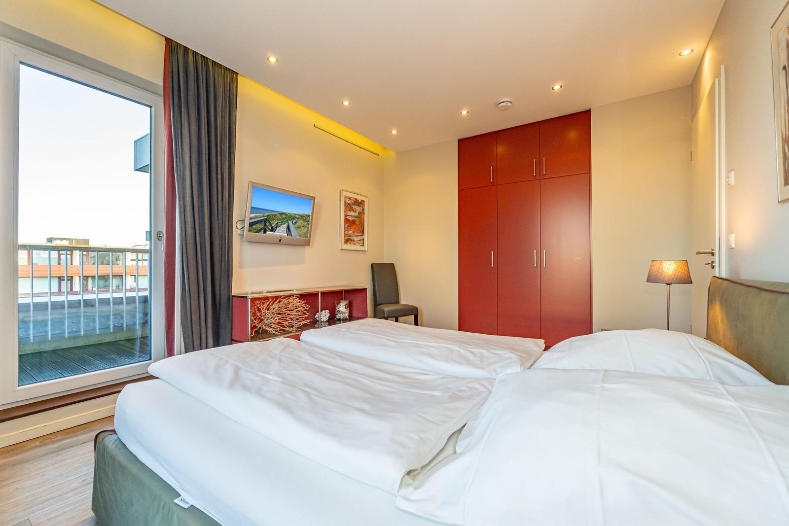 Schlafzimmer mit Doppelbett, rotem Schrank und Balkonansicht.