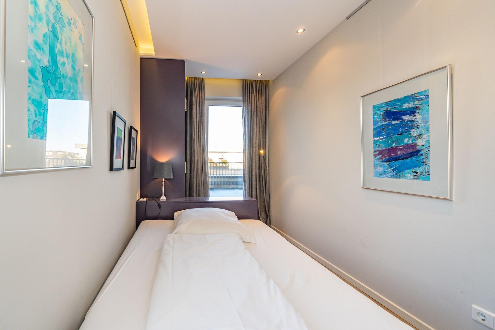 Schlafzimmer mit Bett, Fenster und Wandbildern.