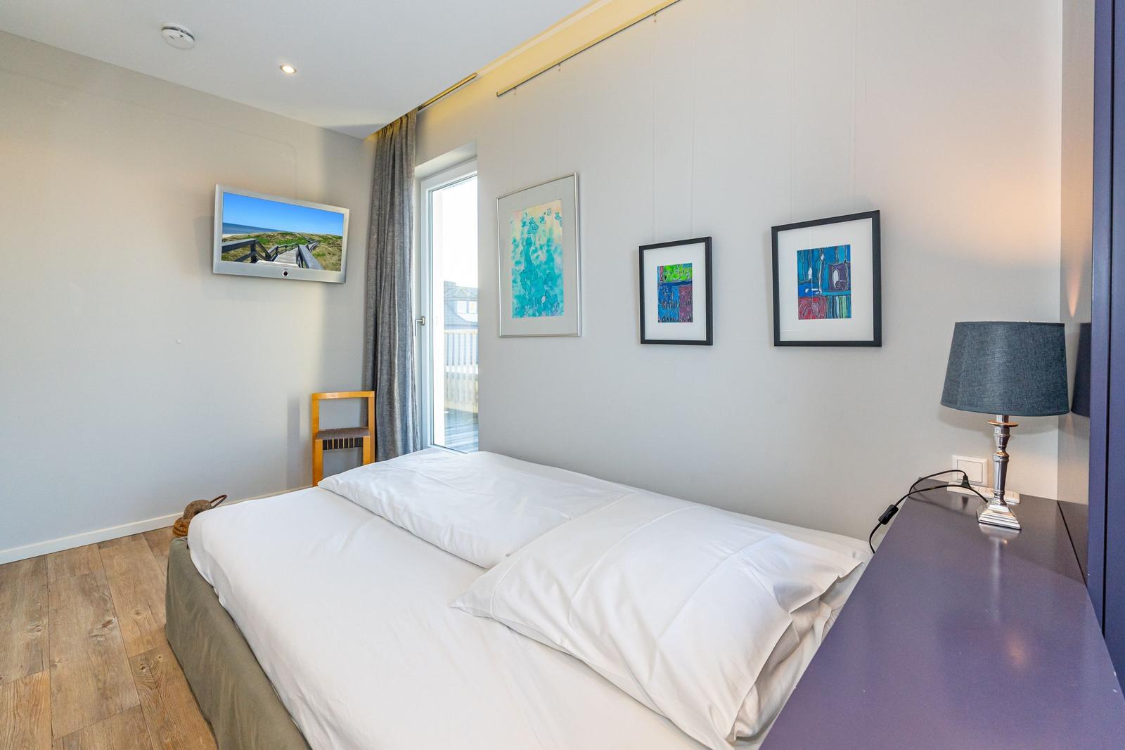 Schlafzimmer mit Bett, Fernseher, Fenster und Bildern an der Wand.