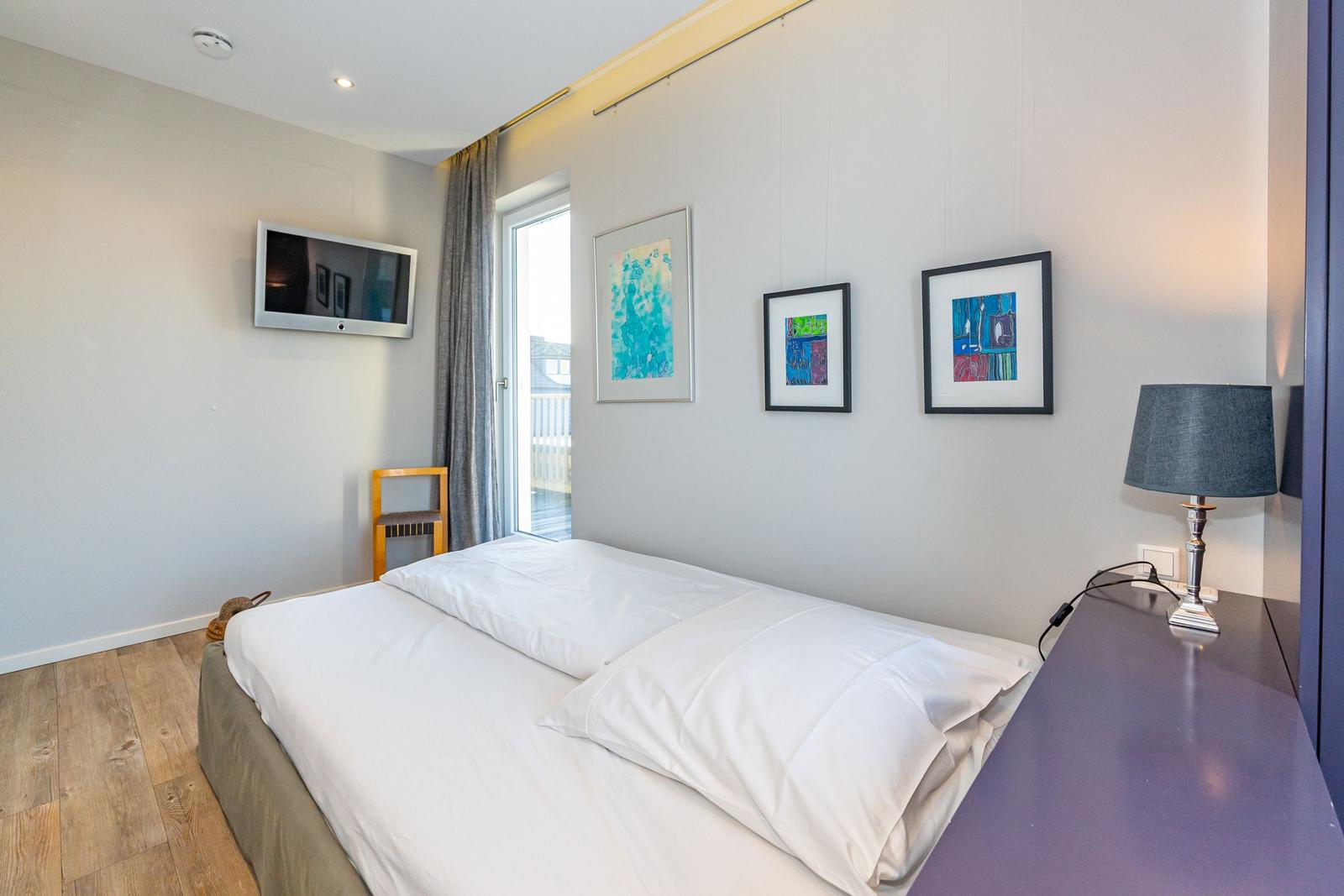 Schlafzimmer mit Bett, Wandbildern, TV und Fenster.