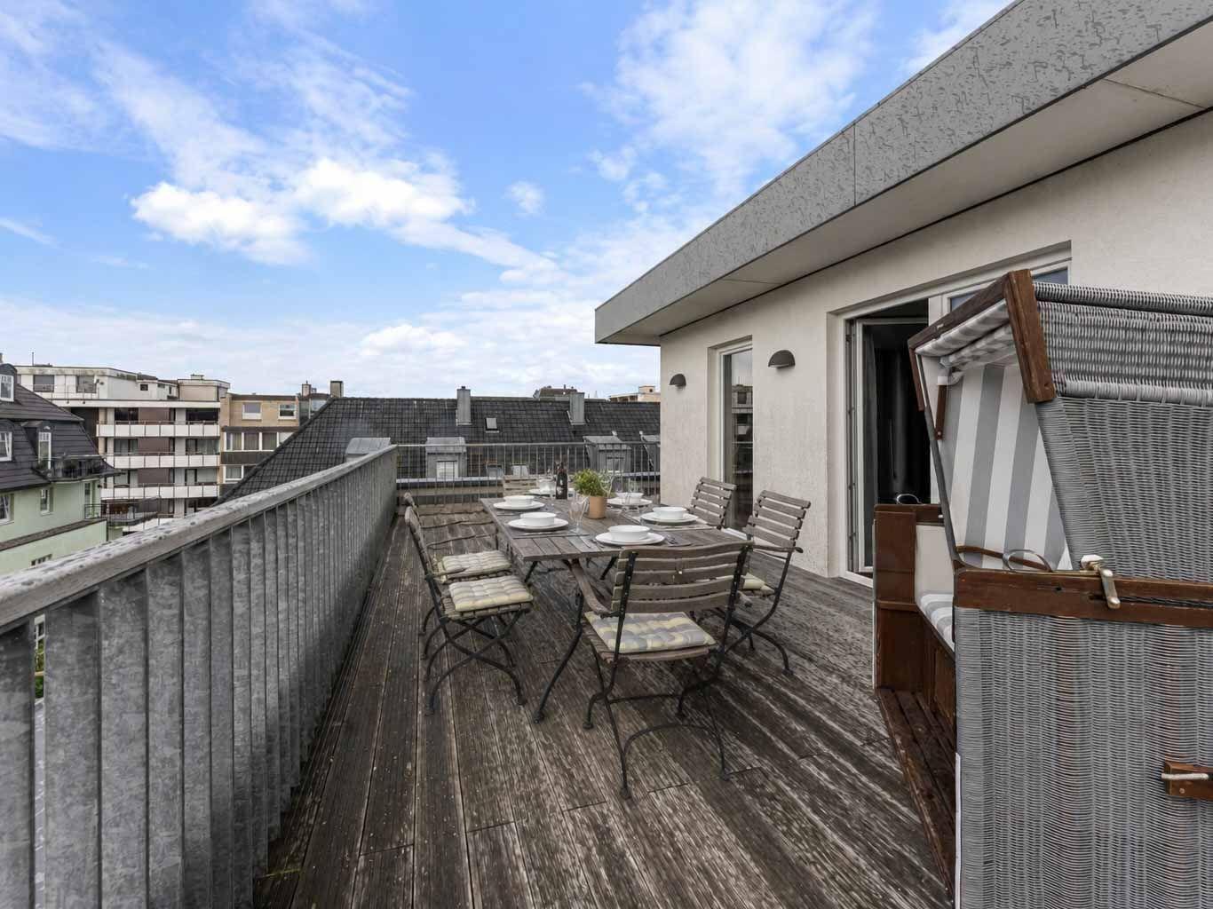 Terrasse mit Tisch, Stühlen und Liegestuhl. Blick auf Stadt und Himmel.