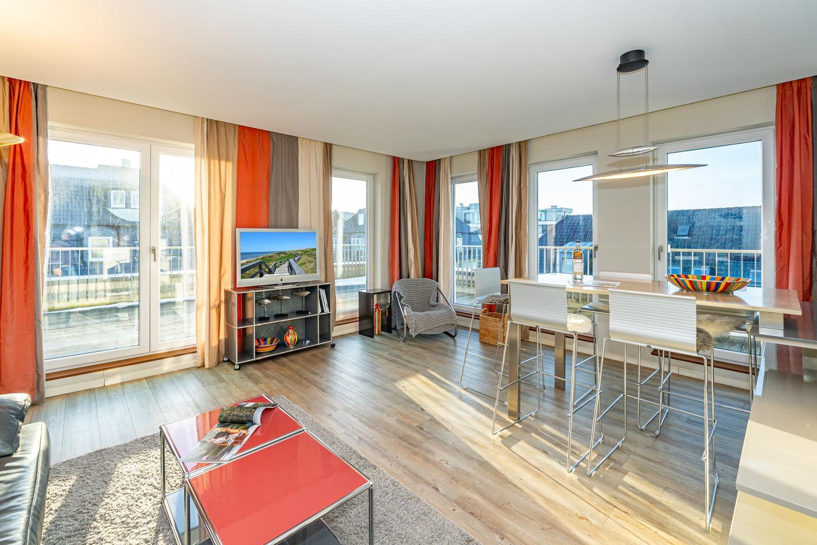 Wohn- und Essbereich mit TV, Balkon und Holzboden. Rote Vorhänge und moderne Möbel.