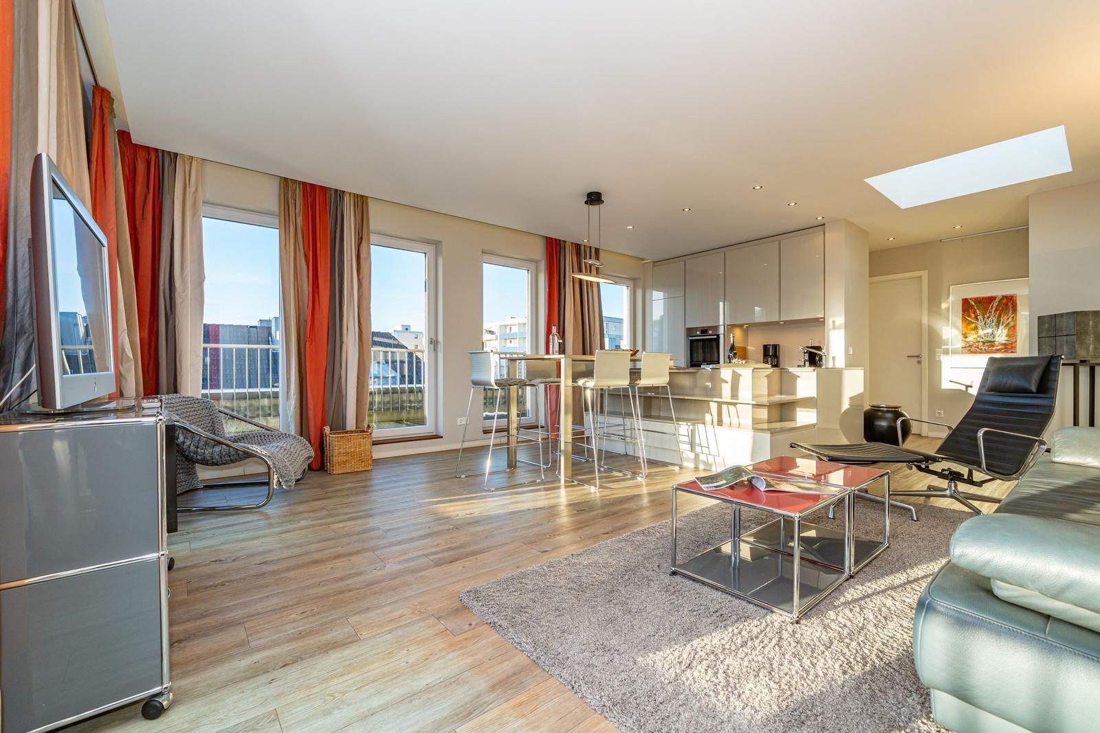 Wohnbereich mit Essbereich, Küche und Balkon. Holzboden, große Fenster und modernes Mobiliar.