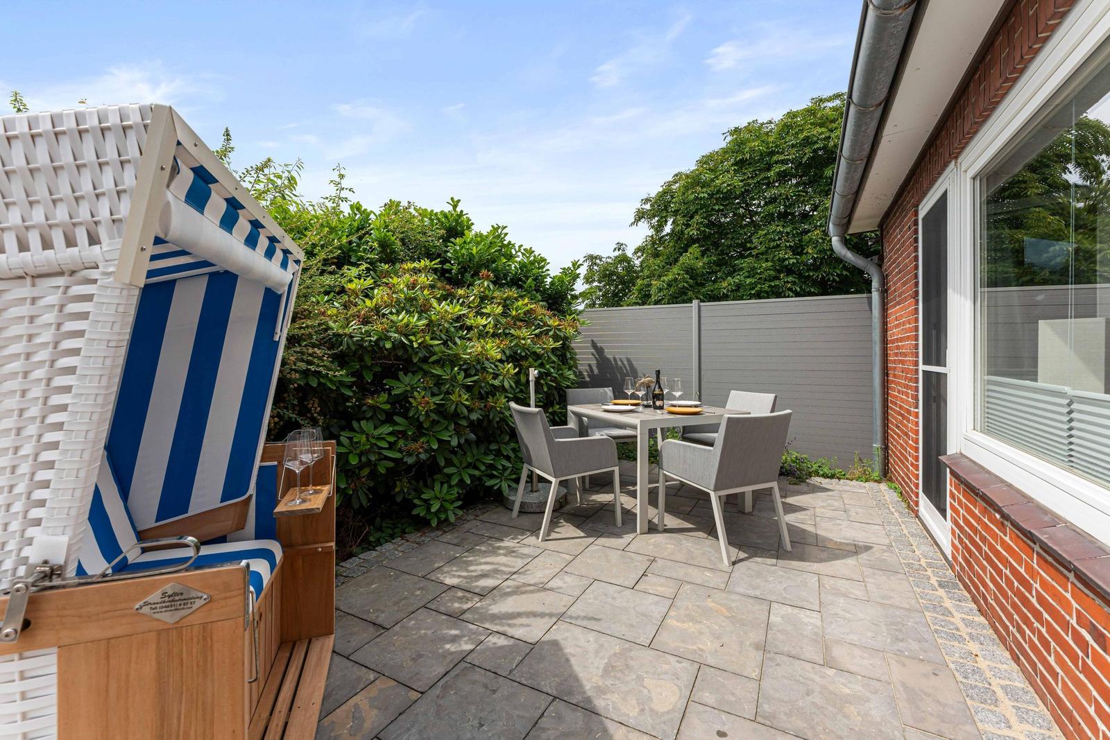 Terrace with beach chair, table and chairs. Backyard with hedge and house wall.
