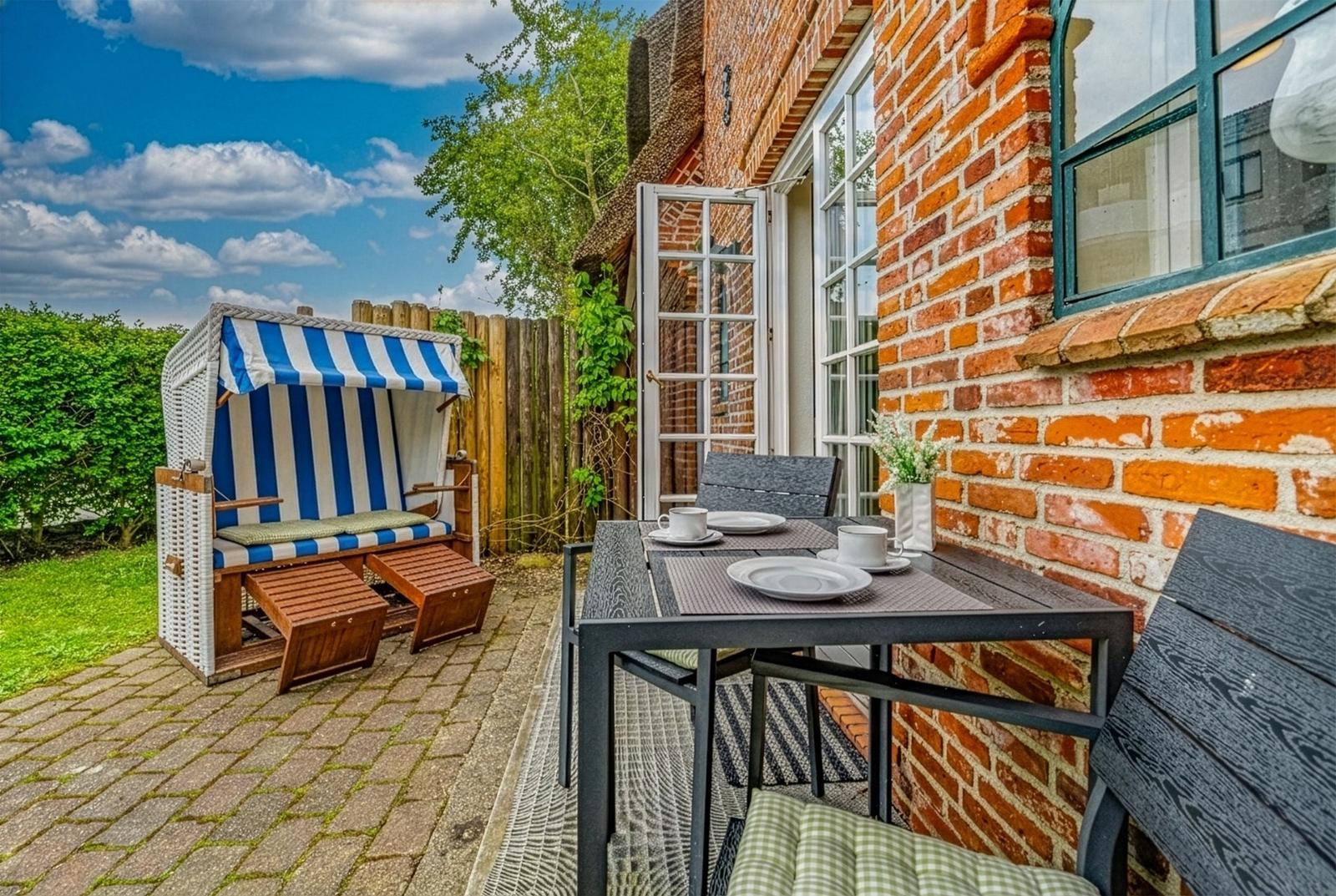 Terrasse mit Tisch, Stühlen und Strandkorb vor Backsteinhaus