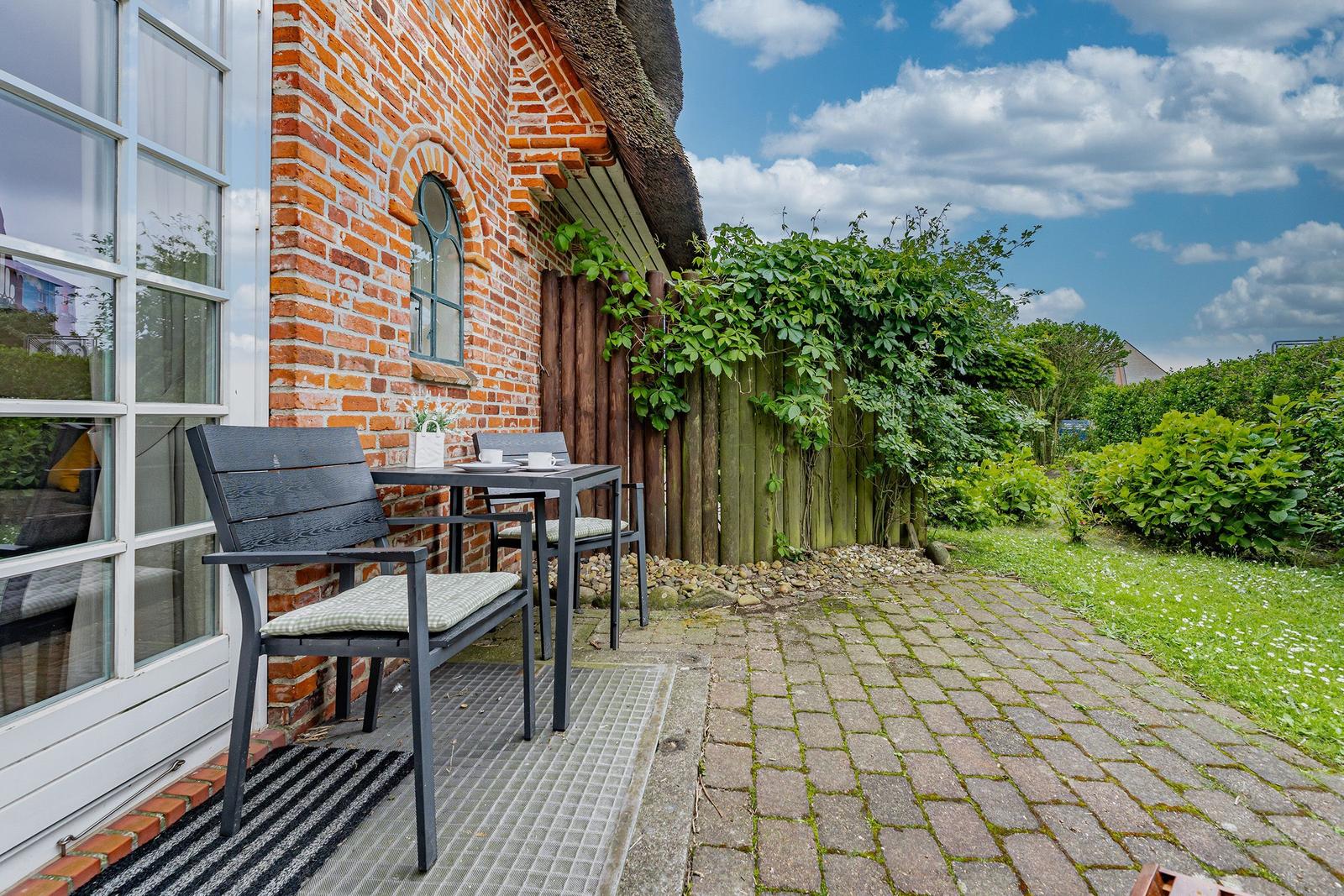 Terrasse mit Tisch und Stühlen vor rotem Backsteinhaus mit Dach aus Stroh