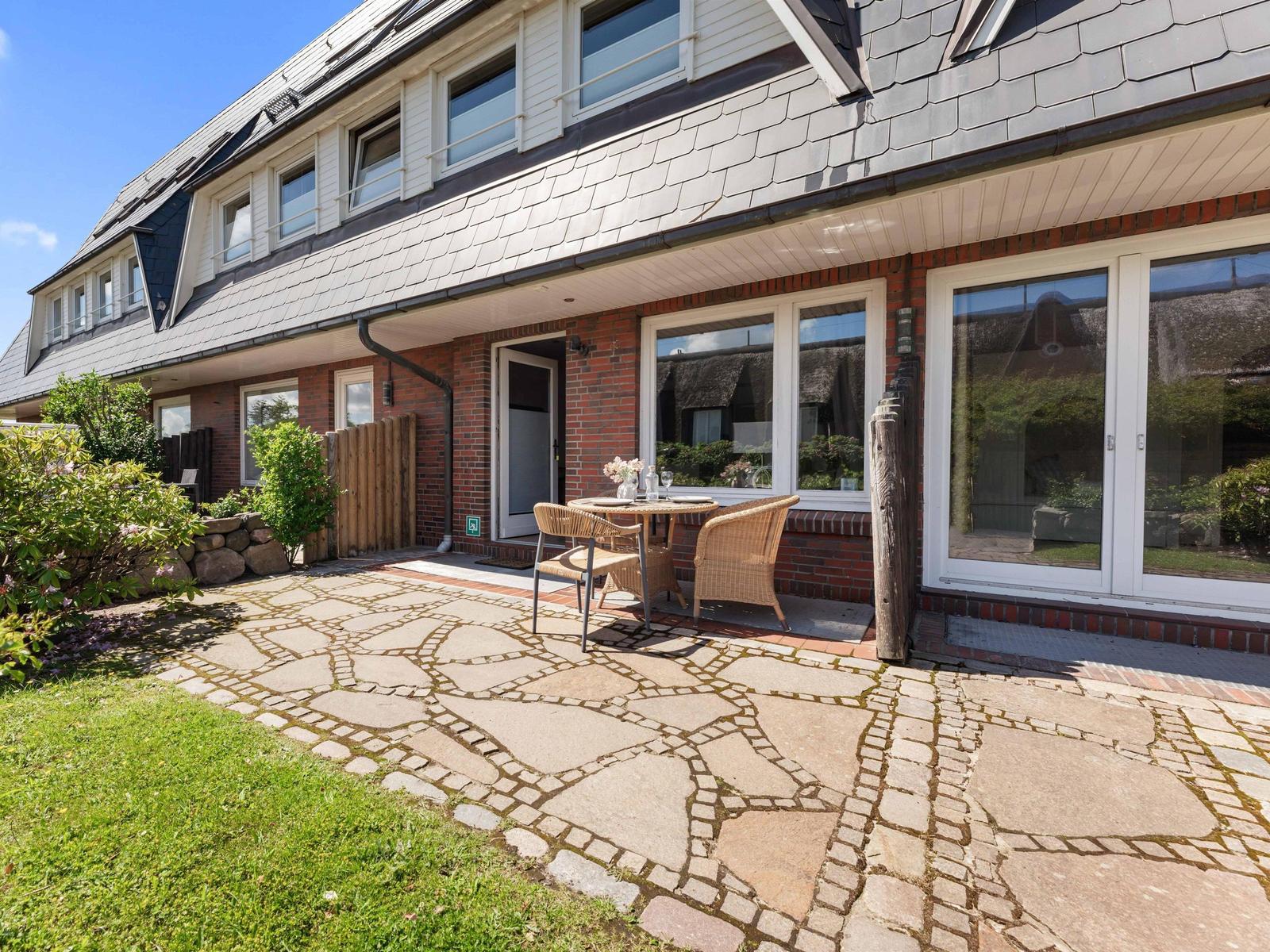 Haus mit Terrasse, Garten und Steinplattenweg. Möblierte Außenterrasse mit Tisch und Stühlen.