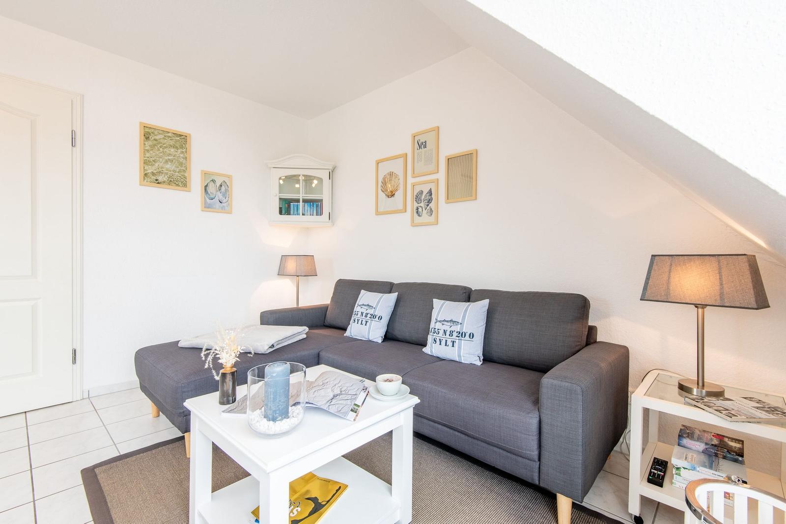 Wohnzimmer mit grauem Sofa, weißen Möbeln und Wandbildern an der schrägen Decke.