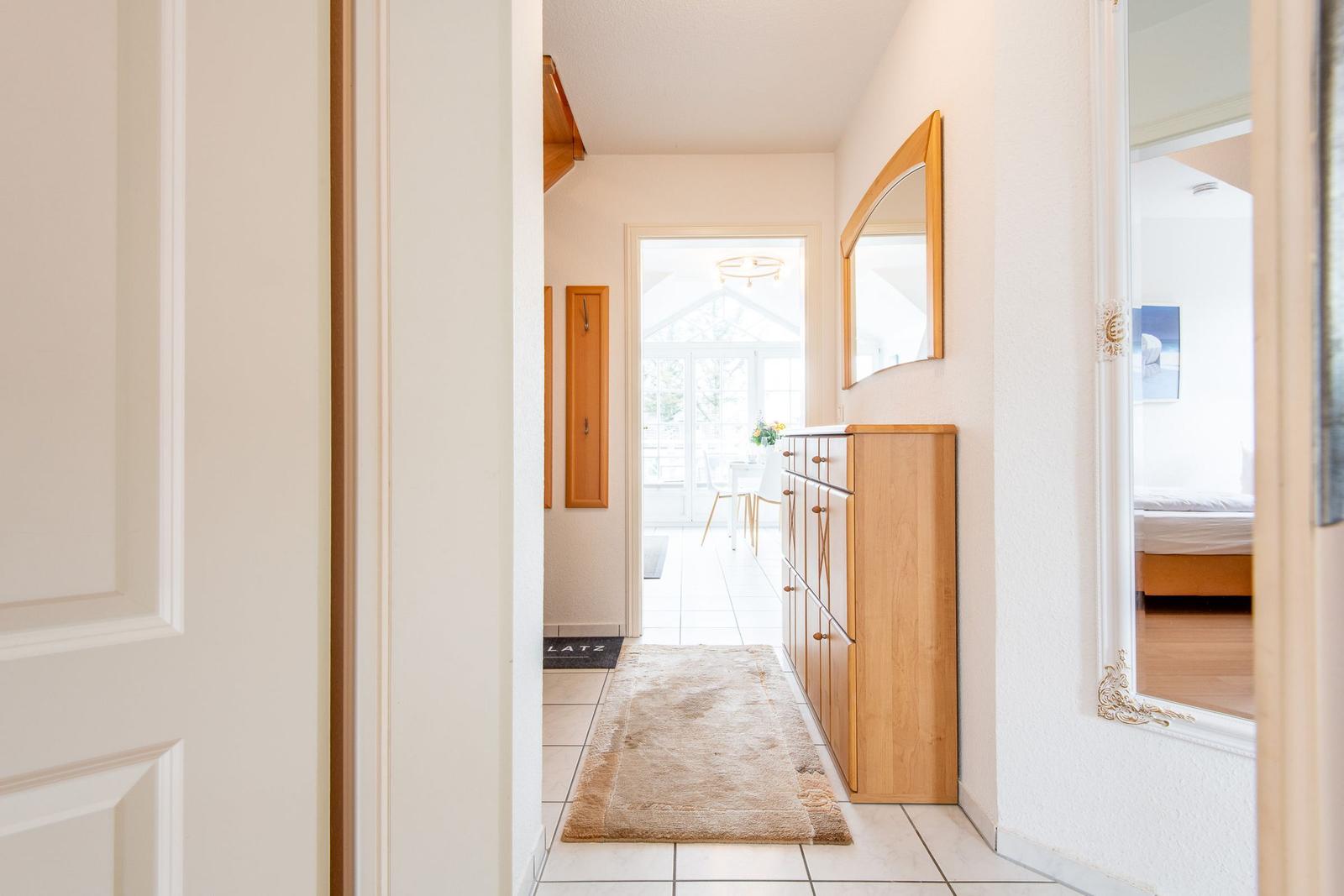 Flur mit Holzschrank, Spiegel und Blick in Wohn- und Schlafzimmer.