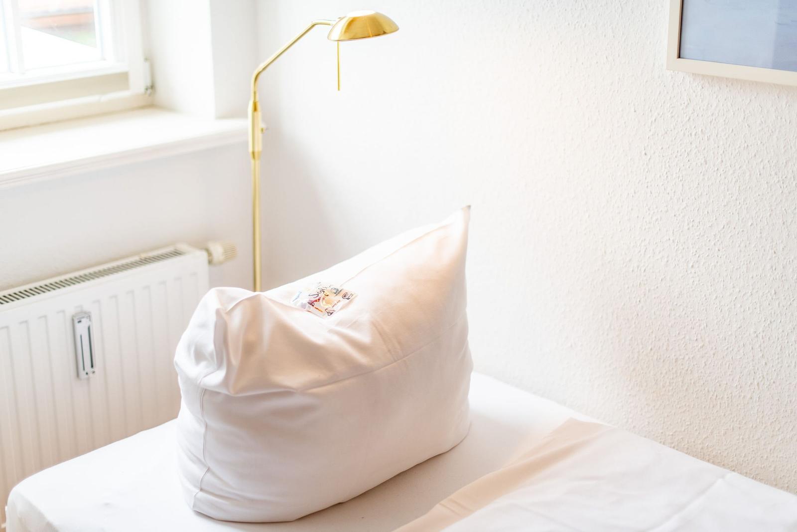 Ein Bett mit Kissen, daneben Stehlampe und Fenster