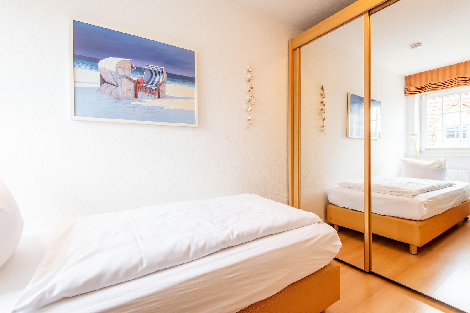 Schlafzimmer mit Bett, Spiegelschrank und Strandgemälde an der Wand.