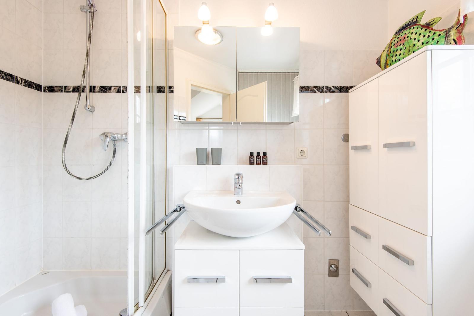 Badezimmer mit Dusche, Waschbecken und Schrank. Dekoratives Fischobjekt auf dem Schrank.