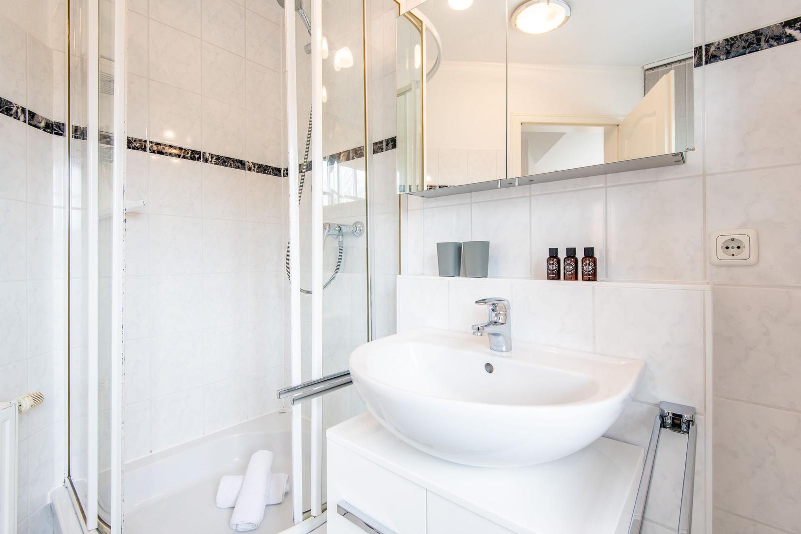 Badezimmer mit Dusche, Waschbecken und Spiegel.