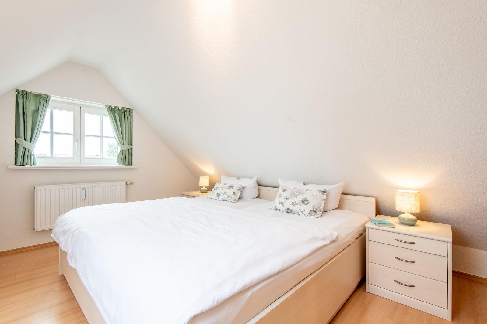 Schlafzimmer mit Doppelbett, Fenster und Nachttischen.