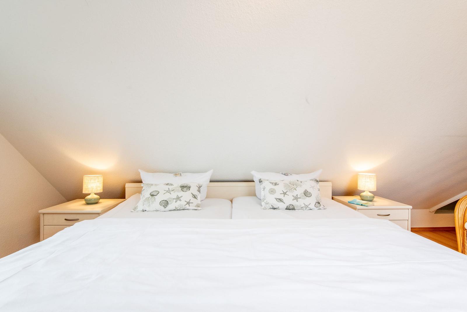 Schlafzimmer mit Doppelbett, zwei Nachttischen und Stehlampen unter schrägen Decken.