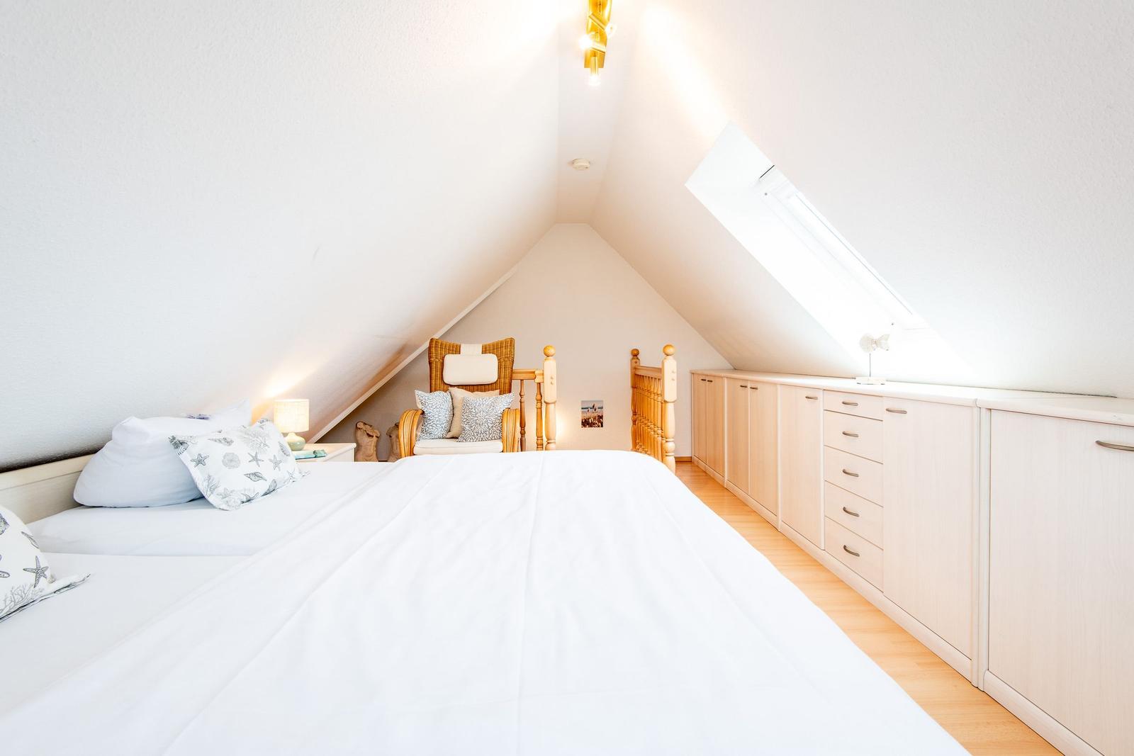 Schlafzimmer mit Dachschräge, Bett, Stuhl und Schränke.