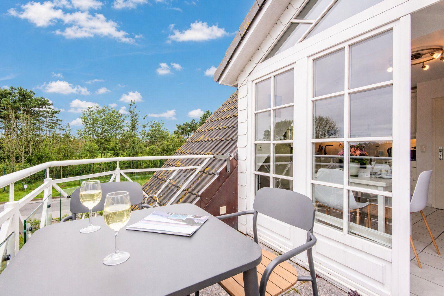 Terrasse mit Tisch, Stühlen und Weingläsern. Blick auf grüne Bäume und blauen Himmel.
