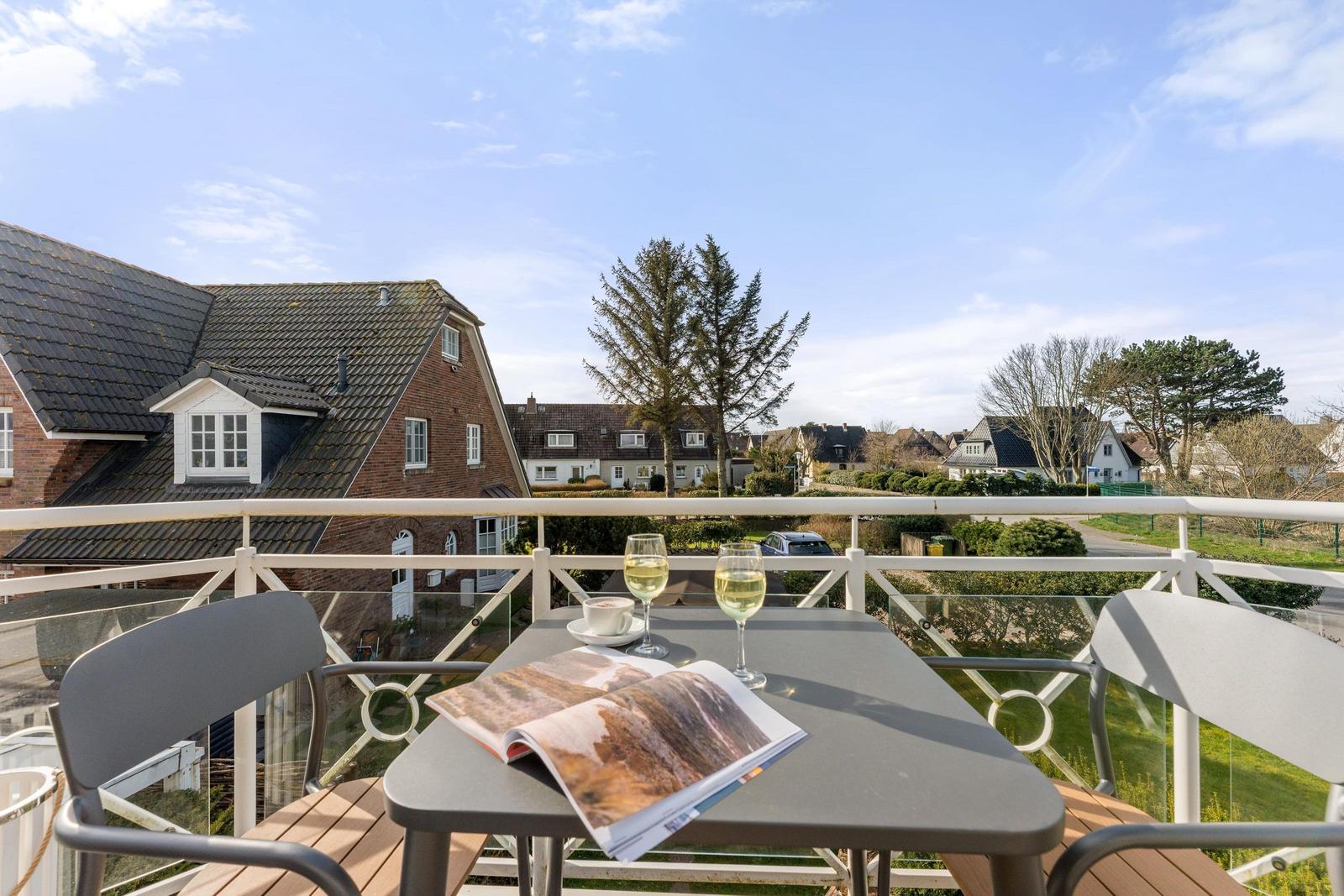 Terrasse mit Tisch, zwei Stühlen, zwei Gläsern Weißwein und einer offenen Zeitschrift.