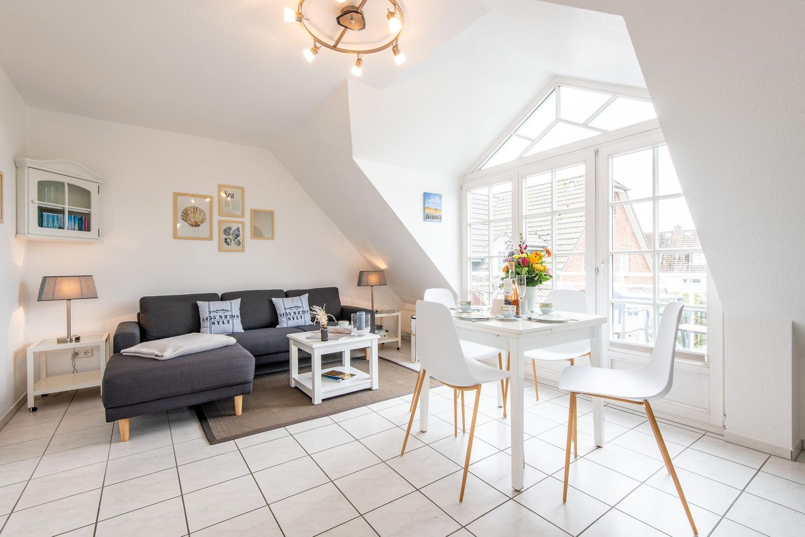 Wohn- und Essbereich mit Sofa, Tisch und Stühlen. Große Fenster und Dachfenster.