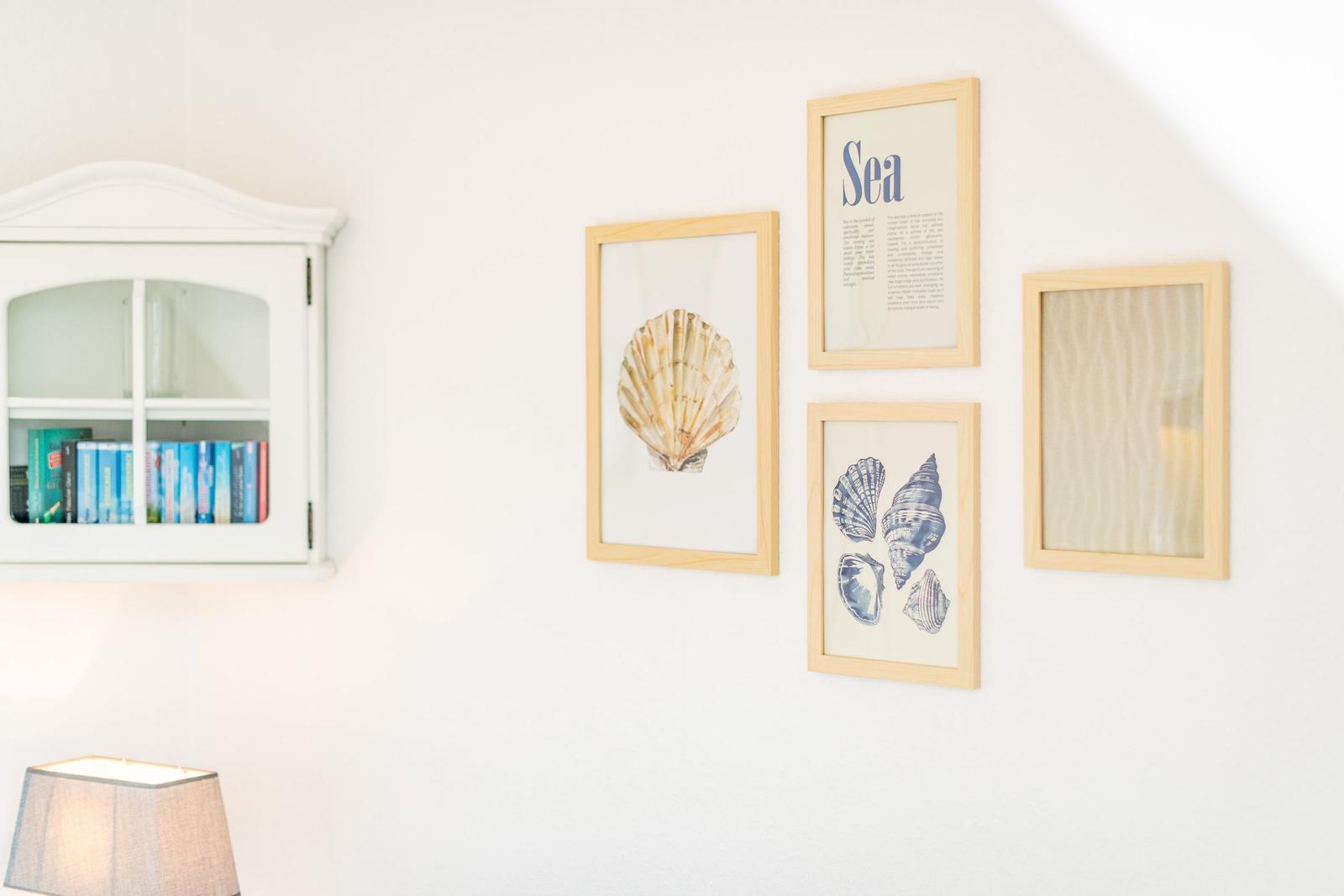 Wand mit vier gerahmten Bildern und einem weißen Schrank mit Büchern.