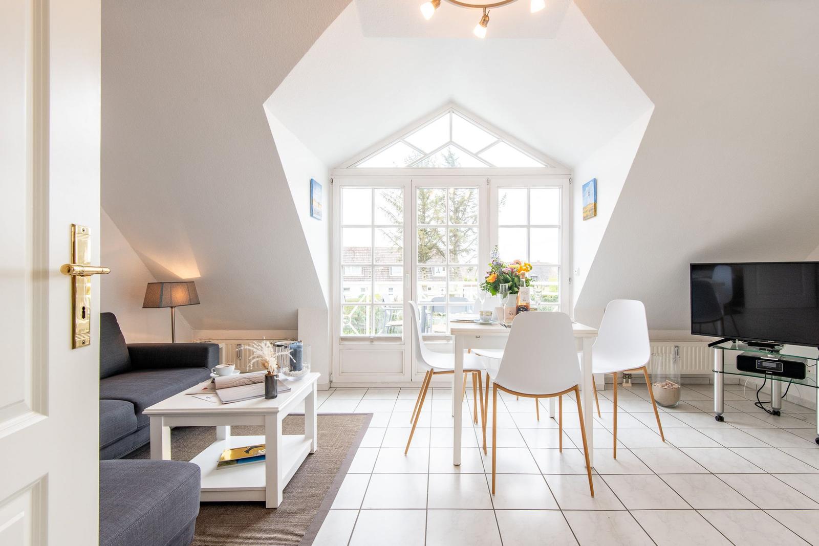 Wohn- und Essbereich mit Sofa, Tisch und Stühlen. Fenster und Dachfenster bieten Licht.