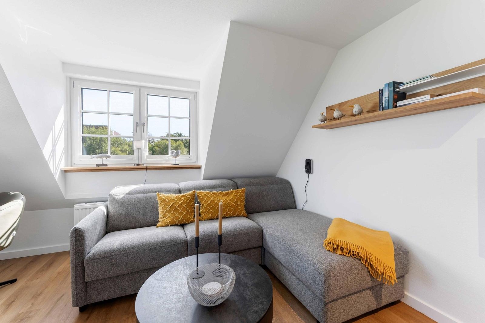 Ein Wohnzimmer mit grauem Sofa, gelben Kissen und einem runden Tisch.