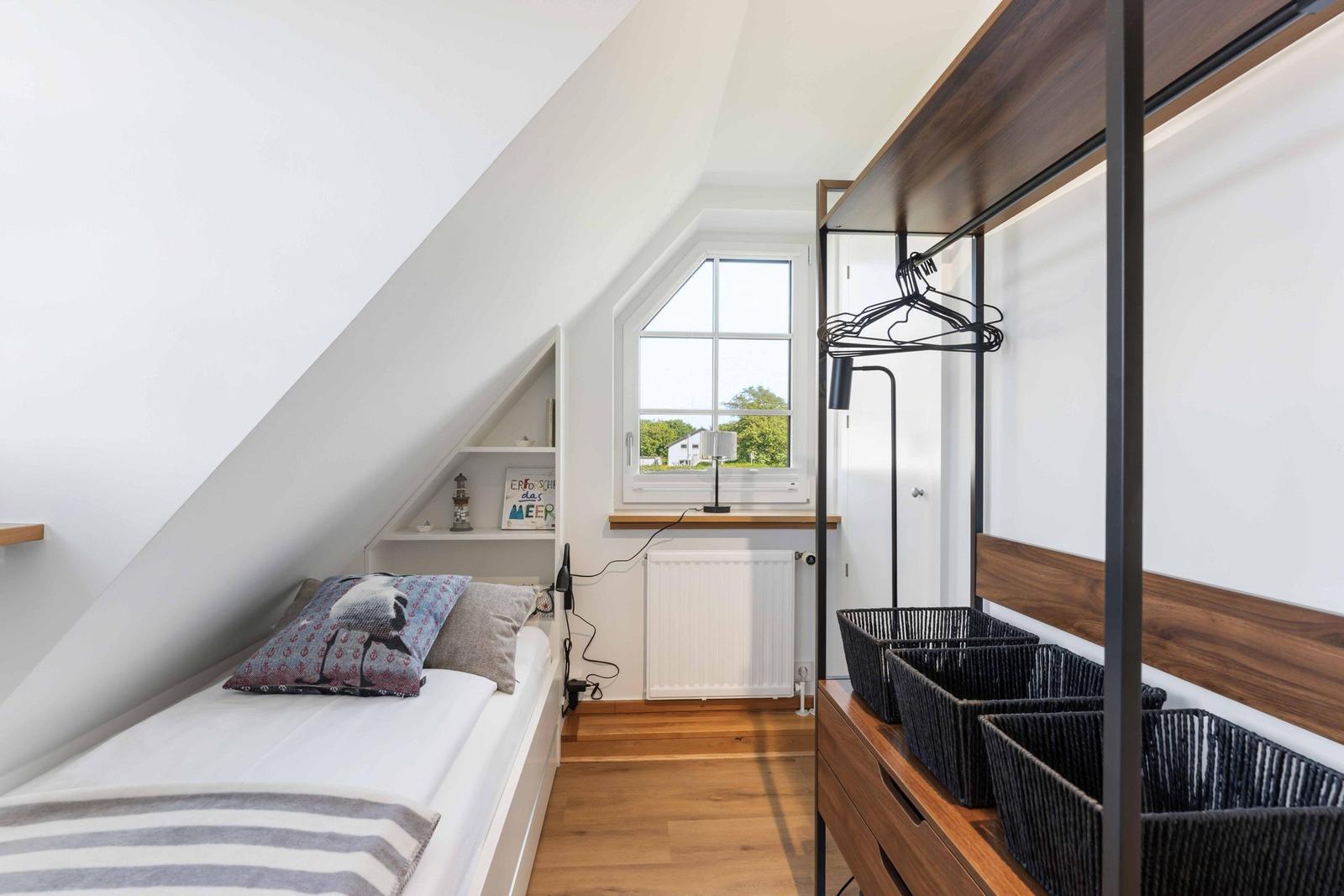 Ein Schlafzimmer mit Dachschrägen, Bett, Kleiderschrank und Fenster mit Blick nach draußen.