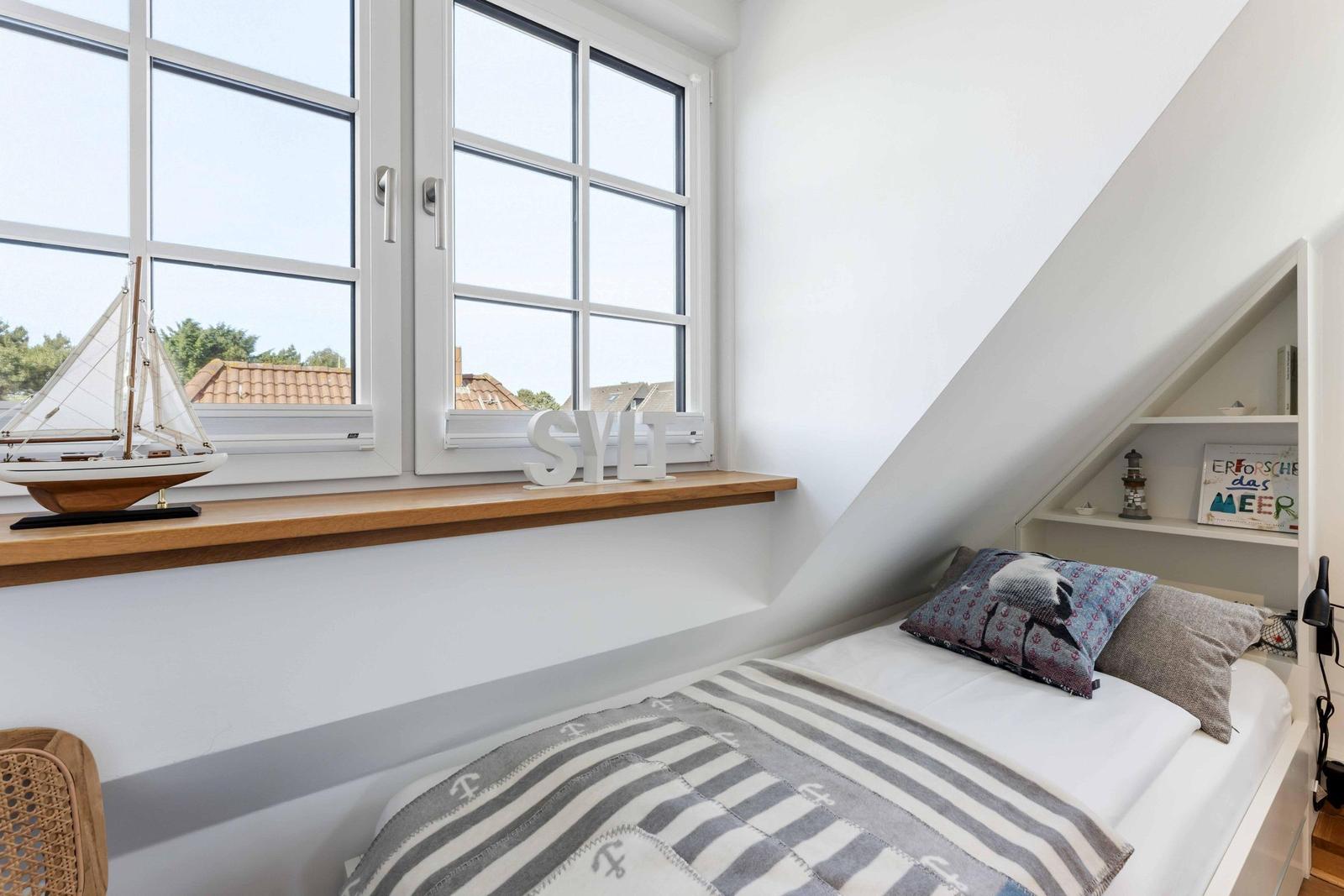 Schlafzimmer mit Dachschrägen, großem Fenster und Bett mit Streifenüberwurf.