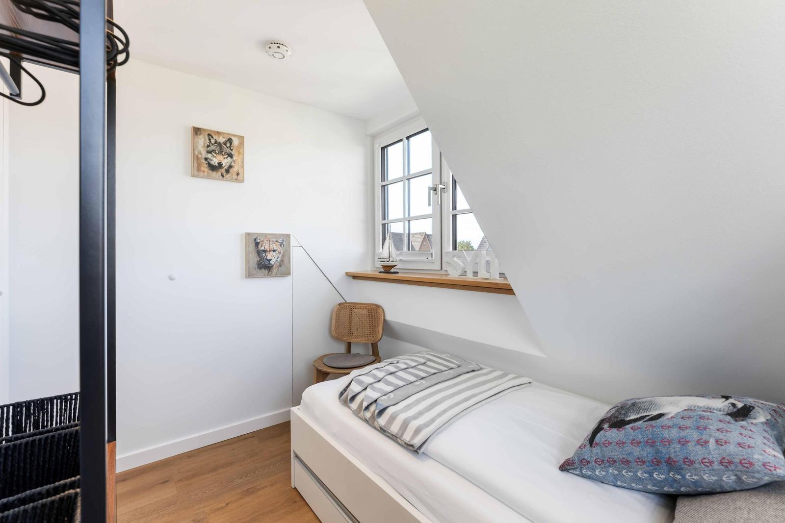Schlafzimmer mit Bett, Fenster und Wandbildern.