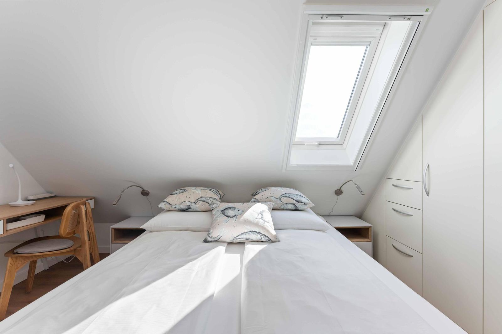 Schlafzimmer mit Dachfenster, Bett, Schreibtisch und Kleiderschrank.