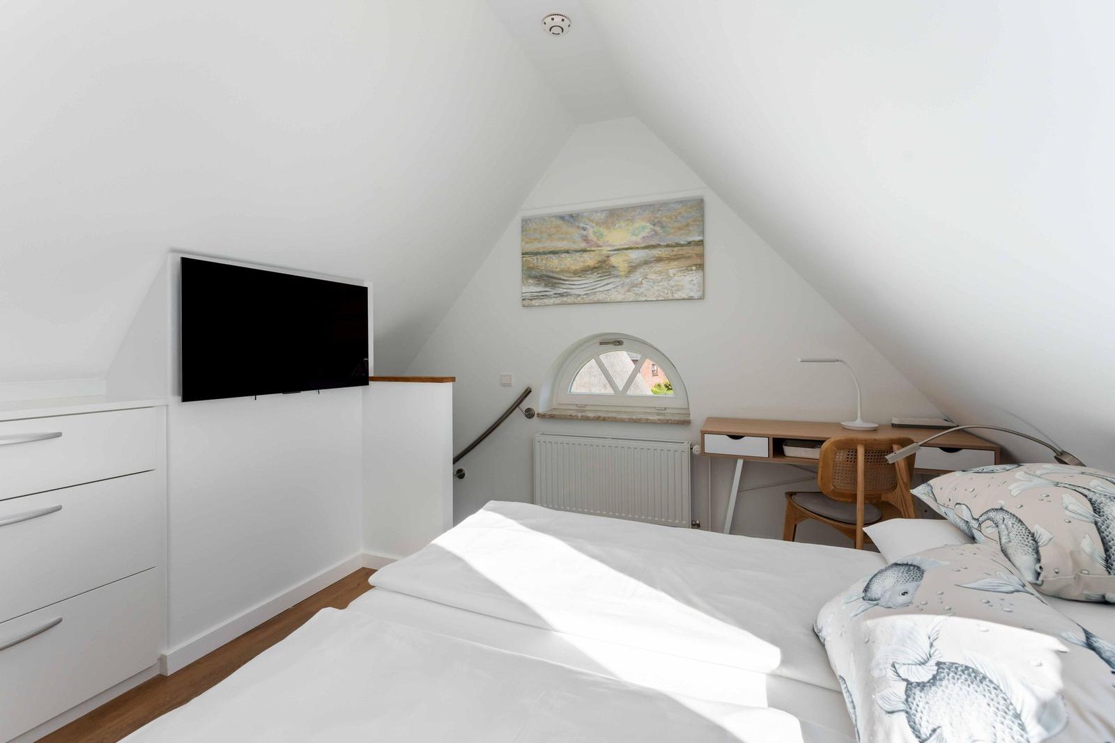 Schlafzimmer mit Dachschrägen, Bett, Schreibtisch und Fernseher an der Wand.