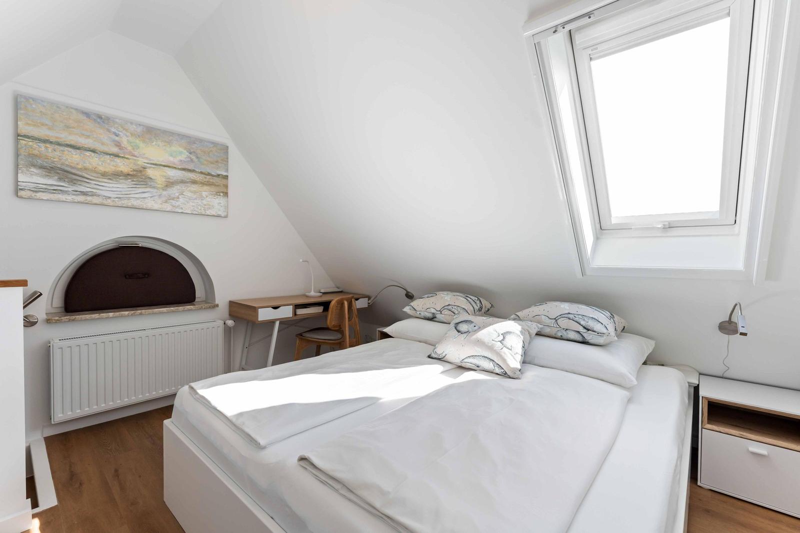 Schlafzimmer mit Dachschrägen, Bett, Schreibtisch und Fenster.
