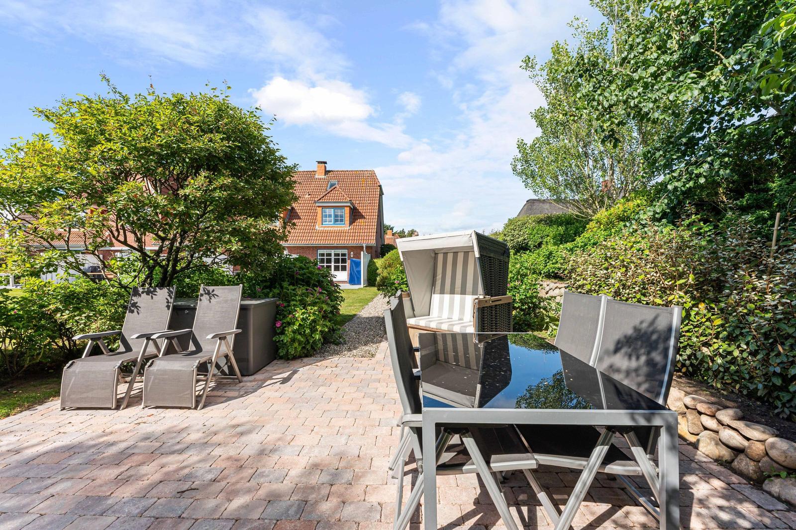 Garten mit Liegestühlen, Tisch und Beerenkiste. Hintergrund: Haus mit rotem Dach.