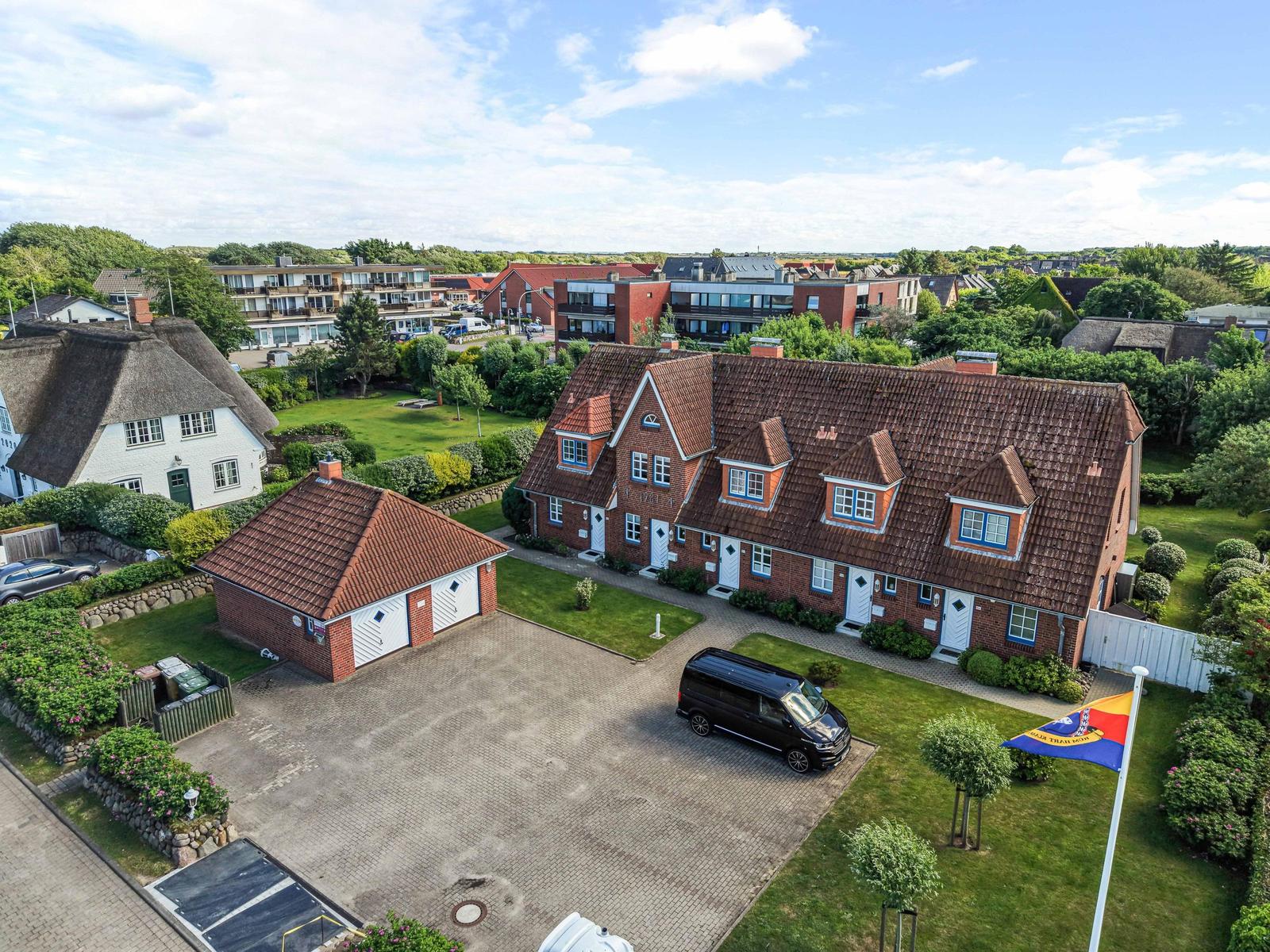 Rotes Backsteinhaus mit Dachgauben und gepflegtem Garten. Parkplatz mit schwarzer Van.