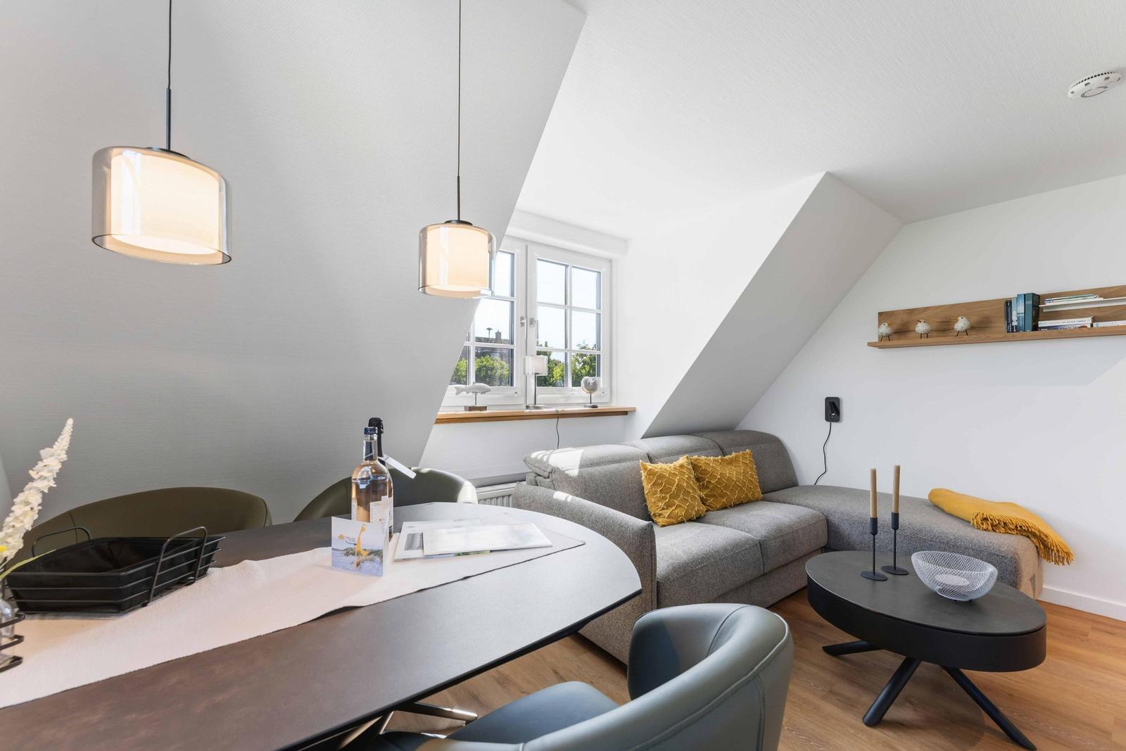 Wohn- und Essbereich mit Sofa, Tisch und Hängelampen unter schrägen Dachdecken.