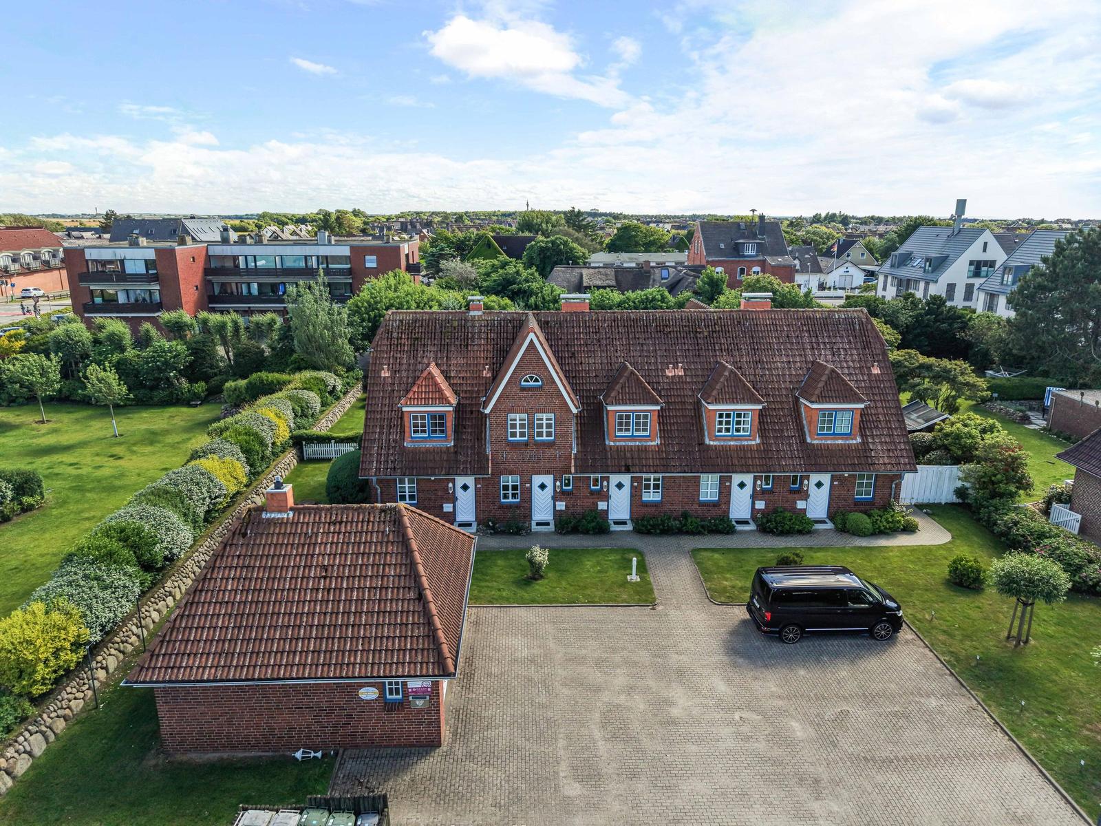 Roter Ziegelbau mit Dachgauben und gepflastertem Hof. Schwarzes Auto parkt vorne.