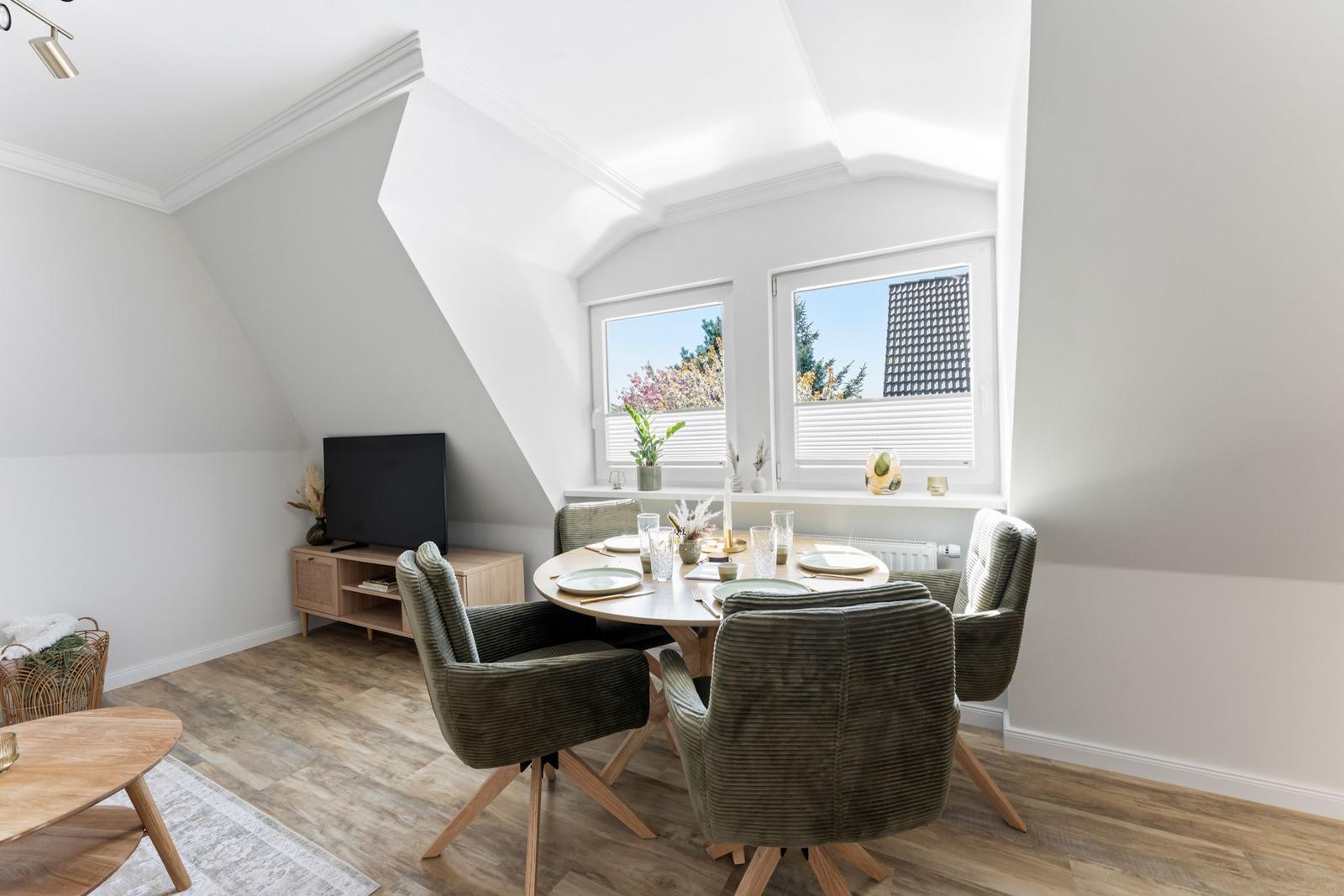 Dining room with round table, four chairs, and two windows. Wooden floor and TV corner.