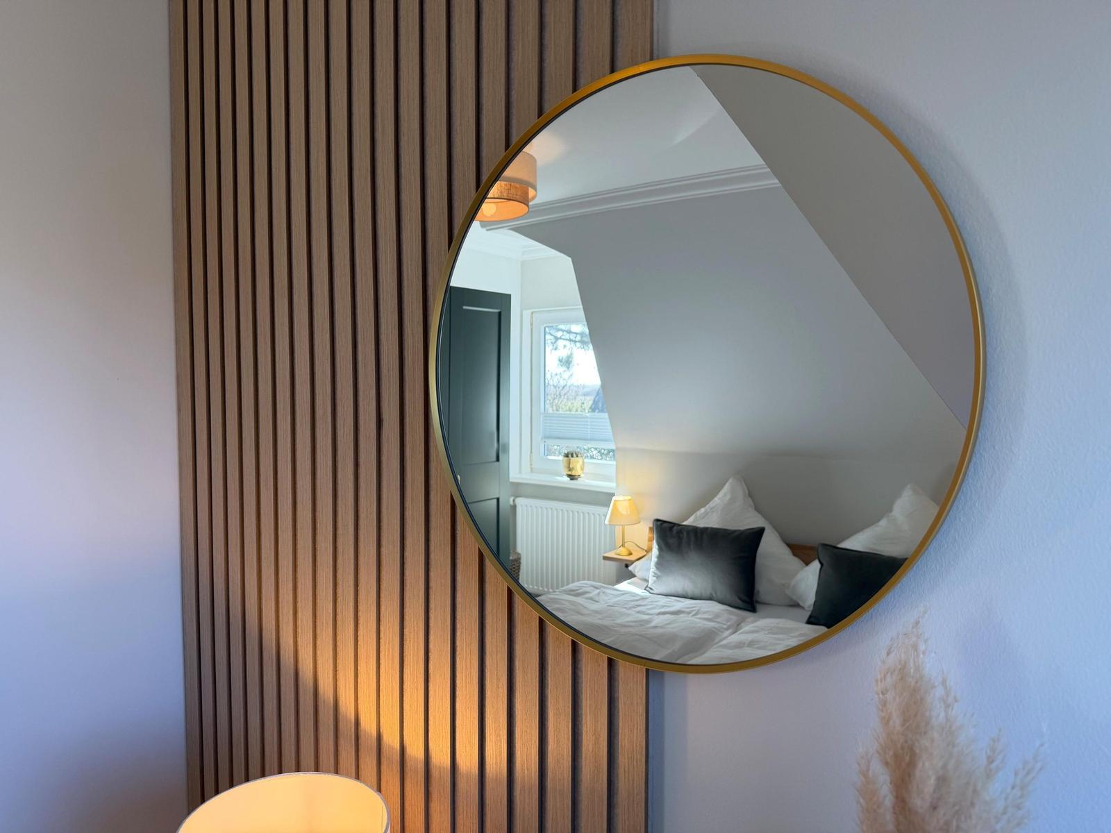 Round mirror with gold frame on wall with wooden verticals.