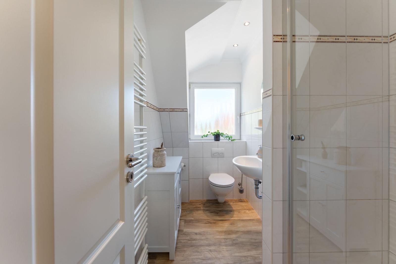 Bathroom with shower, sink, and toilet. Wooden floor and white tile flooring.