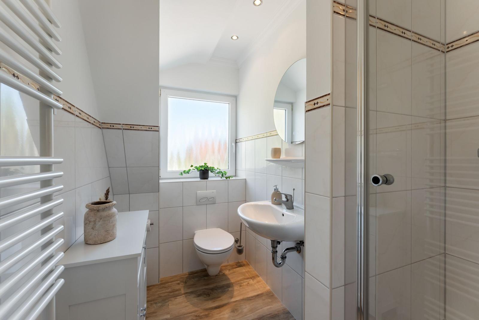 Bathroom with shower, sink, and toilet. Wooden floor and window with plant.