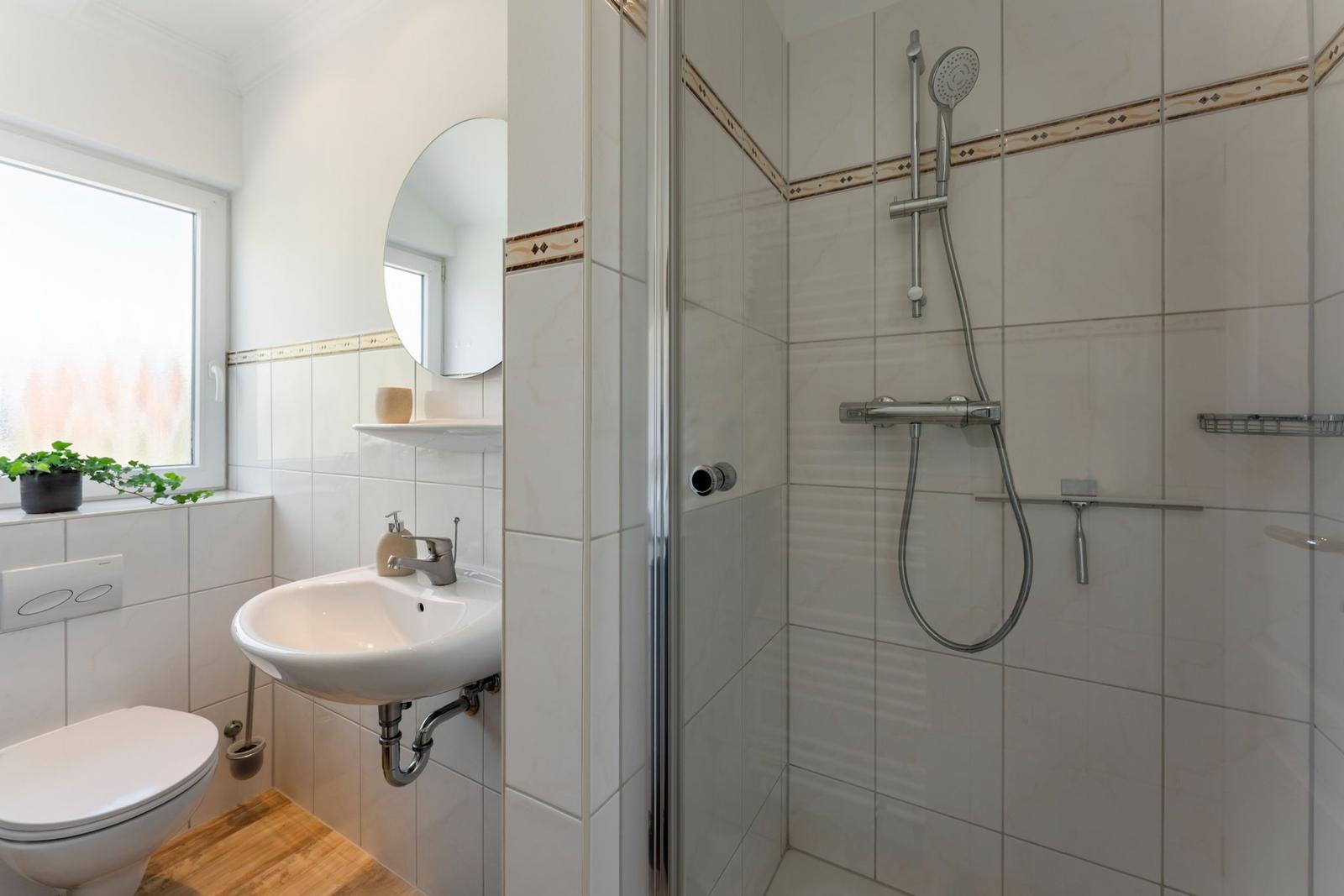 Bathroom with shower, sink, and toilet. Window with plant.