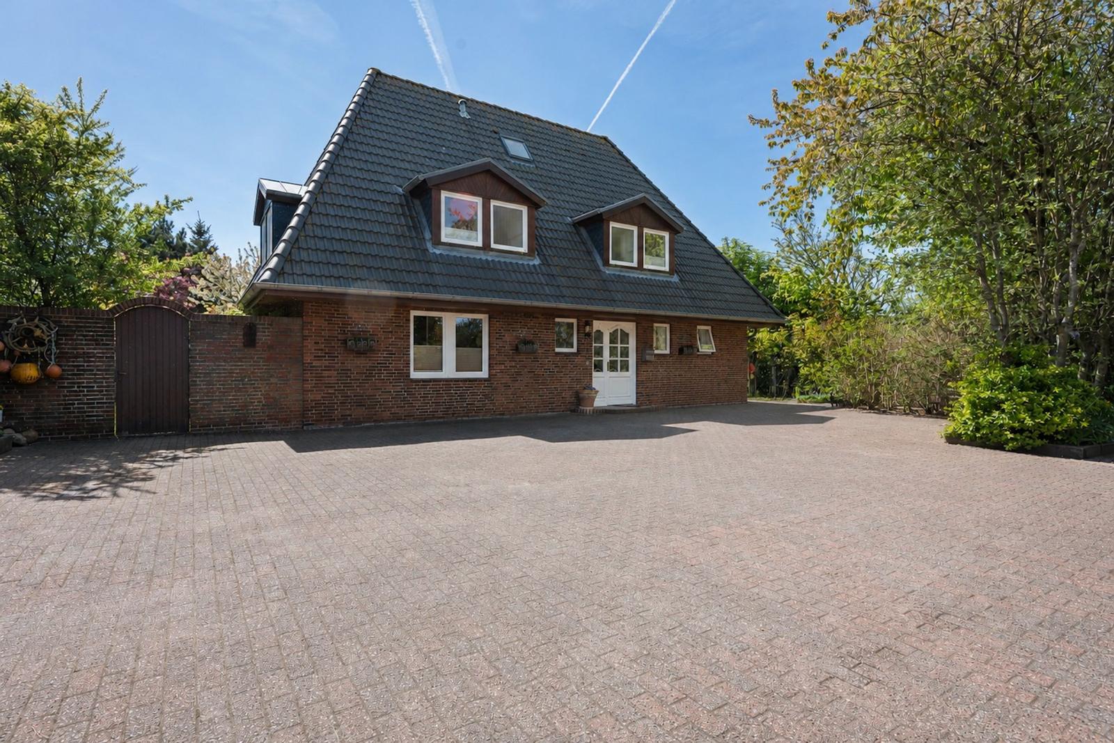 A two-story house with a dark roof and red brick. In front of the house is a paved courtyard.