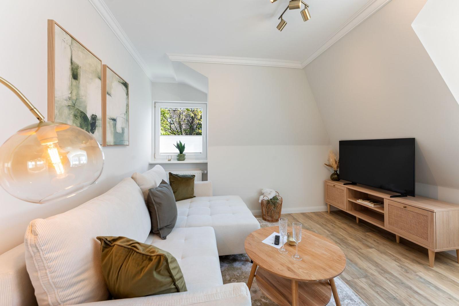 Living room with sofa, TV, and wooden table. Window with view outside.