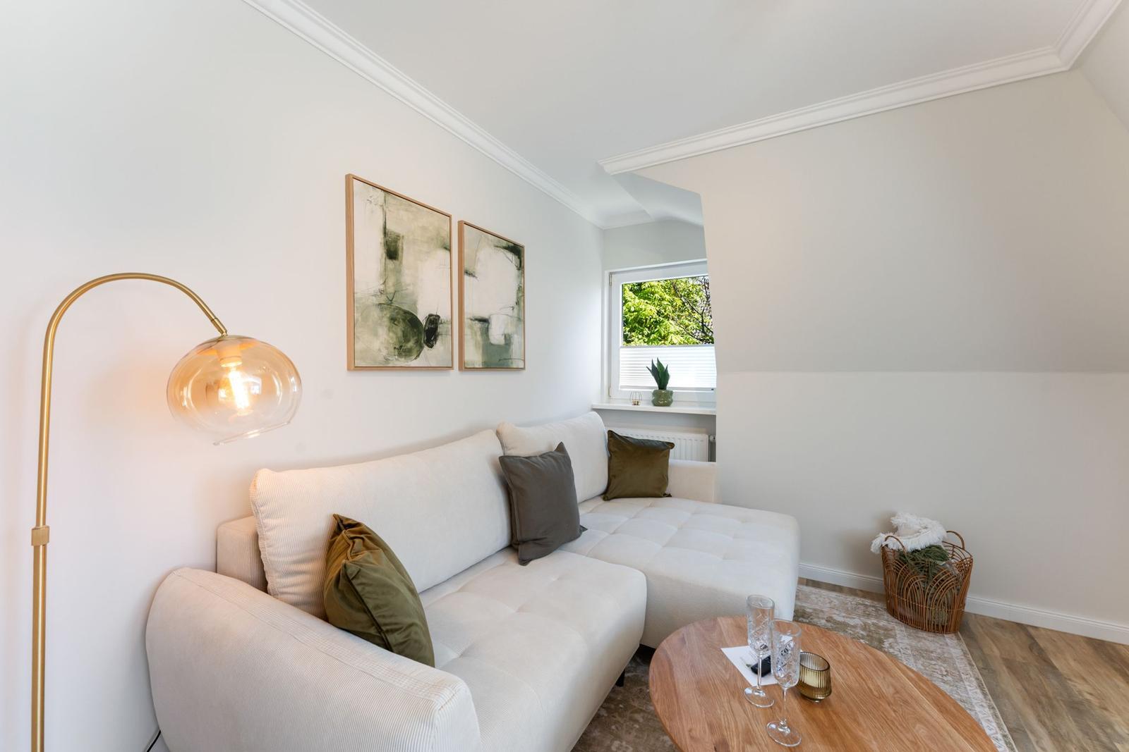 Living room with sofa, table, and window. Wall art and floor lamp visible.