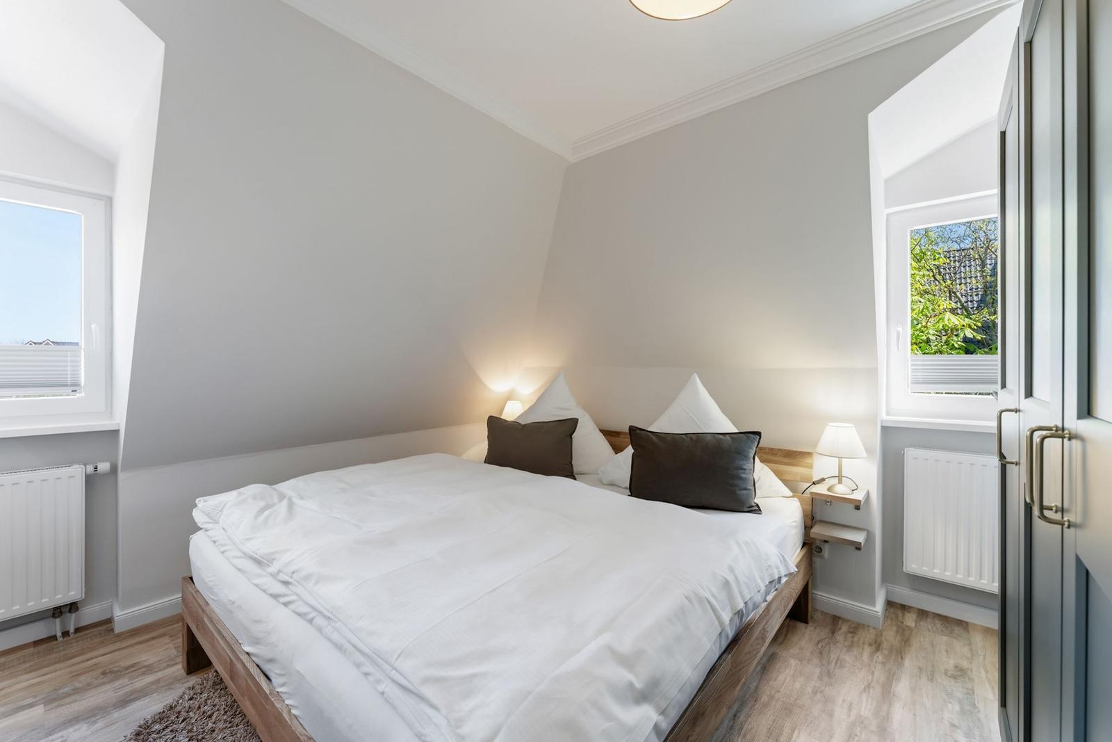 Bedroom with double bed, two windows, and wooden floor.