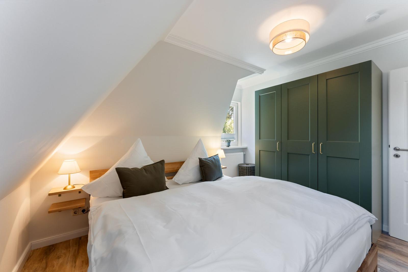 Bedroom with bed, green wardrobe, and nightstand under sloped ceiling.